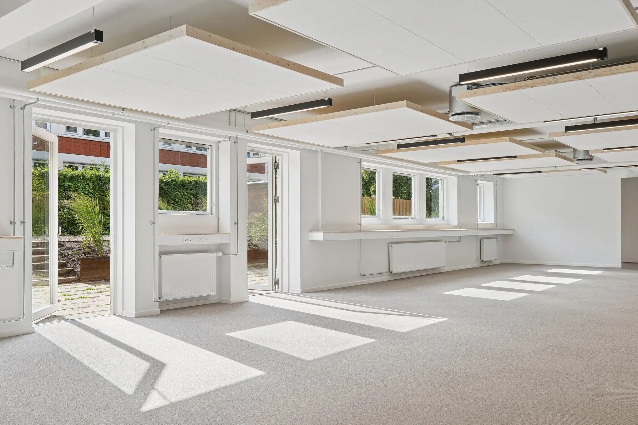 Moderne, hvidt interiør med store glasdøre og vinduer, højt til loftet, og lyse, lyse gulve. Hjørner med plantepotter og