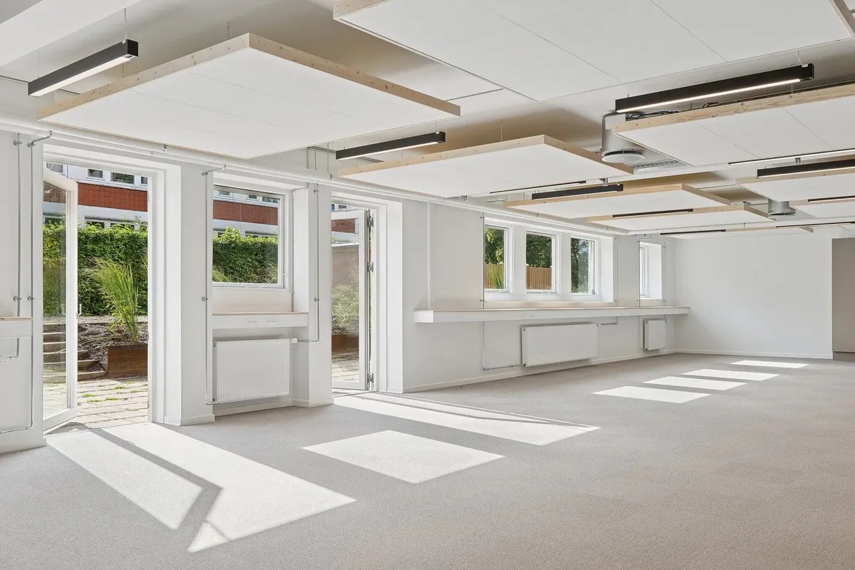 Moderne, hvidt interiør med store glasdøre og vinduer, højt til loftet, og lyse, lyse gulve. Hjørner med plantepotter og