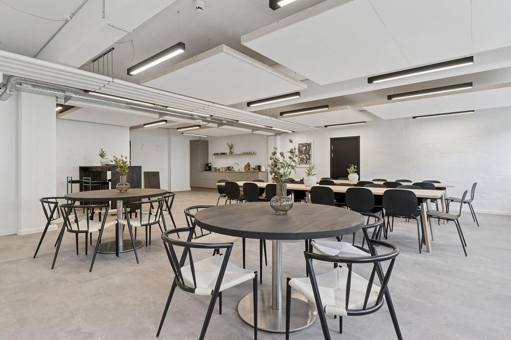 Moderne konferencelokale med runde borde, hvide vægge, højt loft og lysekroner, alle møbler er sorte og hvide