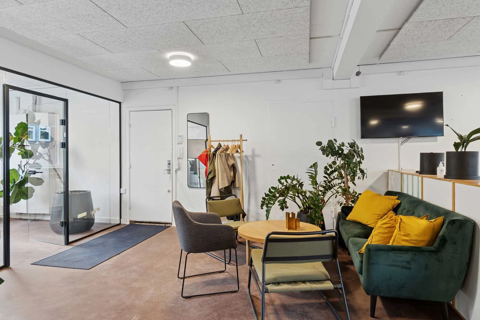 Kontor med grøn sofa, to stole og rundt bord med to stearinlys og plante på loftet