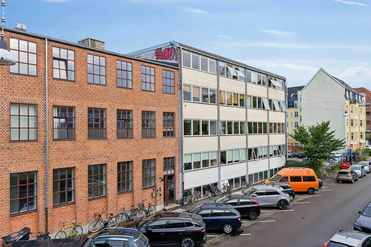 Kontorbyggeri med to rækker røde mursten og hvide vindueskarme, flere biler og en orange varevogn parkeret