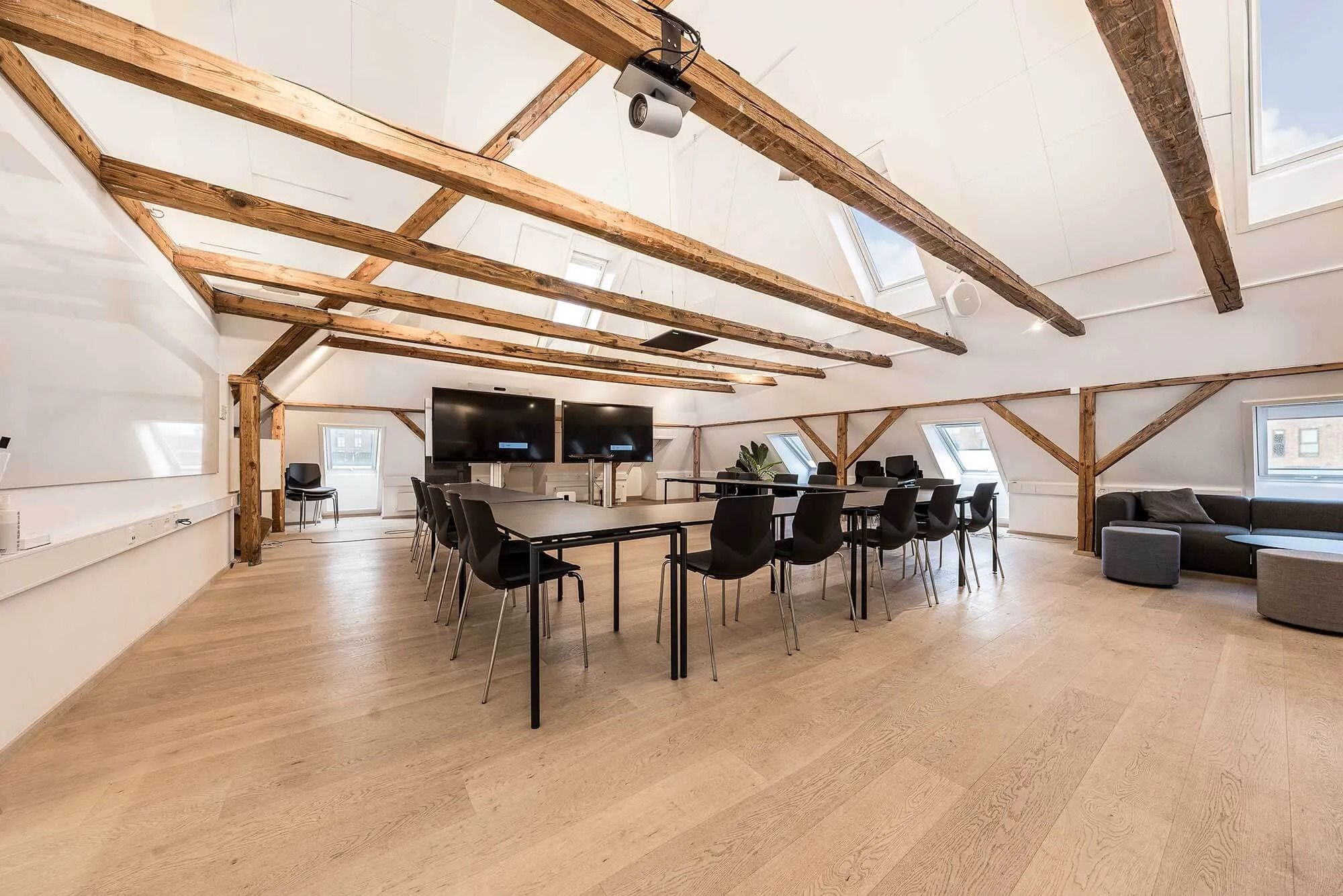 Kontorloft med lyse træbjælker og lyse loftsvinduer samt en stor mødesal med lange borde og stole