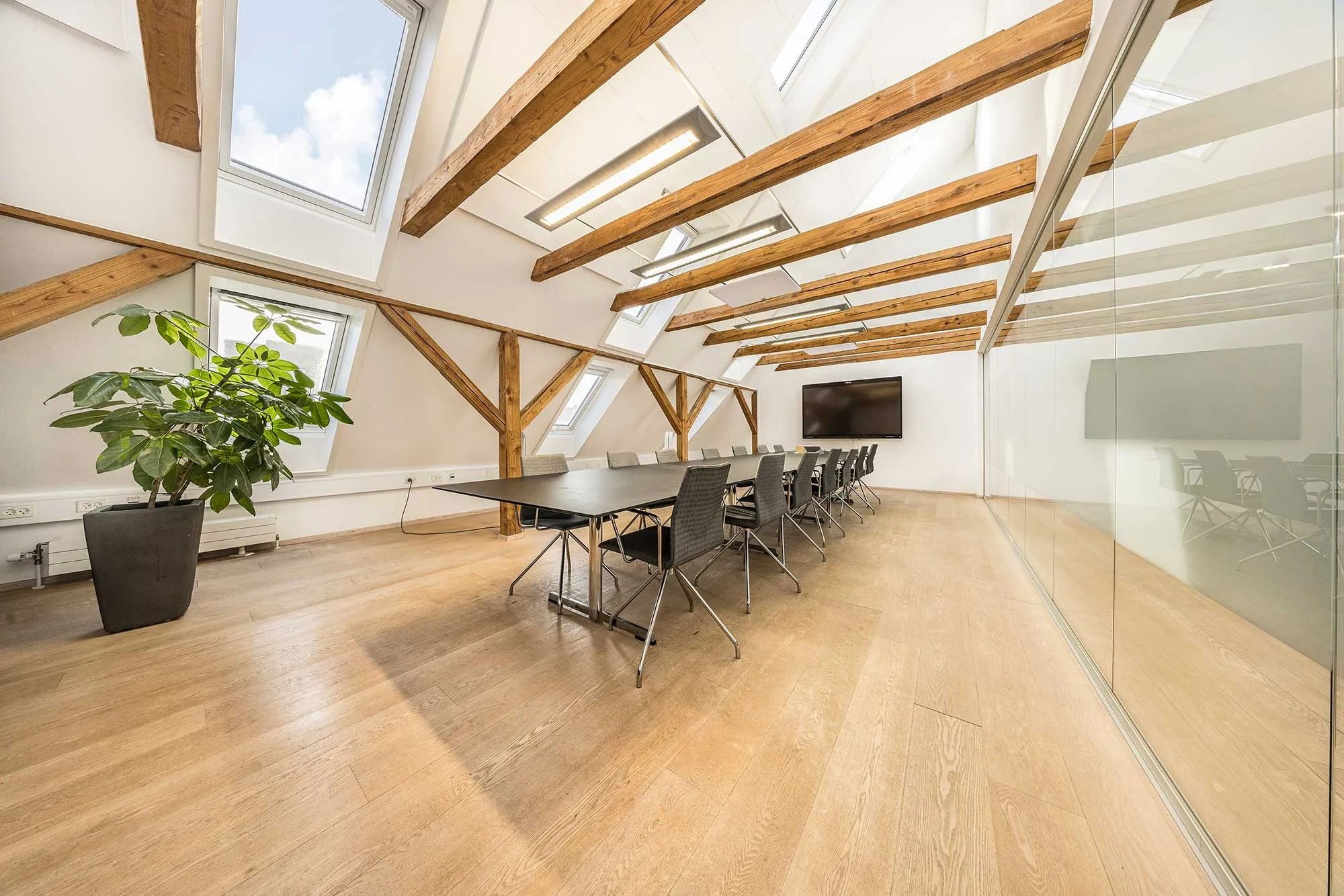 En kontorsal med moderne møbler og træloft, en stor plante og en tv-skærm