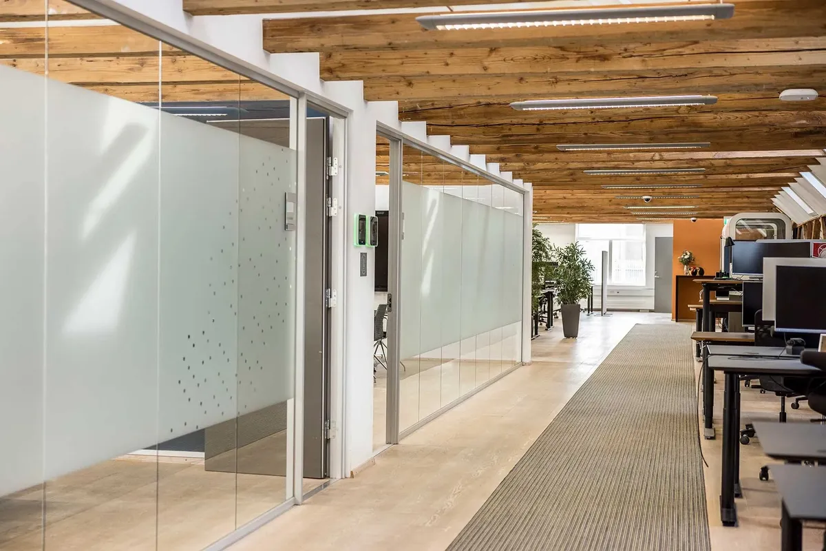 Kontorrum med højt loft, glasvægge og en stor plante i enden af rummet