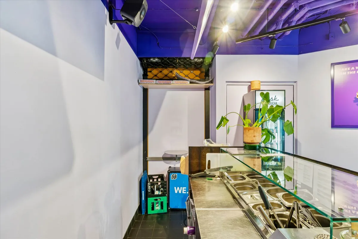 Bag en glasvæg er der et køkken med en stor metalkomfur og en plante i gryden, der reflekteres. Der er også en krukke og et