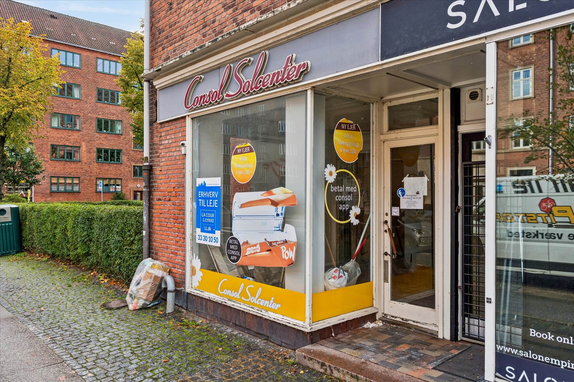 En butik med navnet Consul Solcenter med udsalgsvinduer og en indgangsdør, der er lukket. Butikken ligger på en vej og har