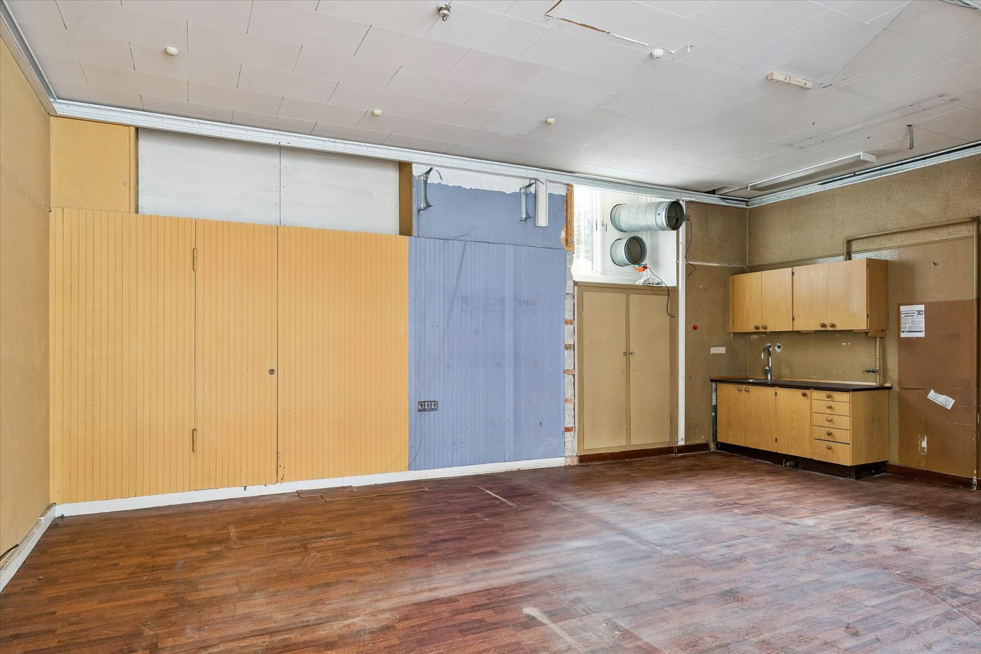 Store rum med lysegul væg og to høje træskabe med hængslede døre, samt en åben dør mod en udstyret køkkenvæg med vask og