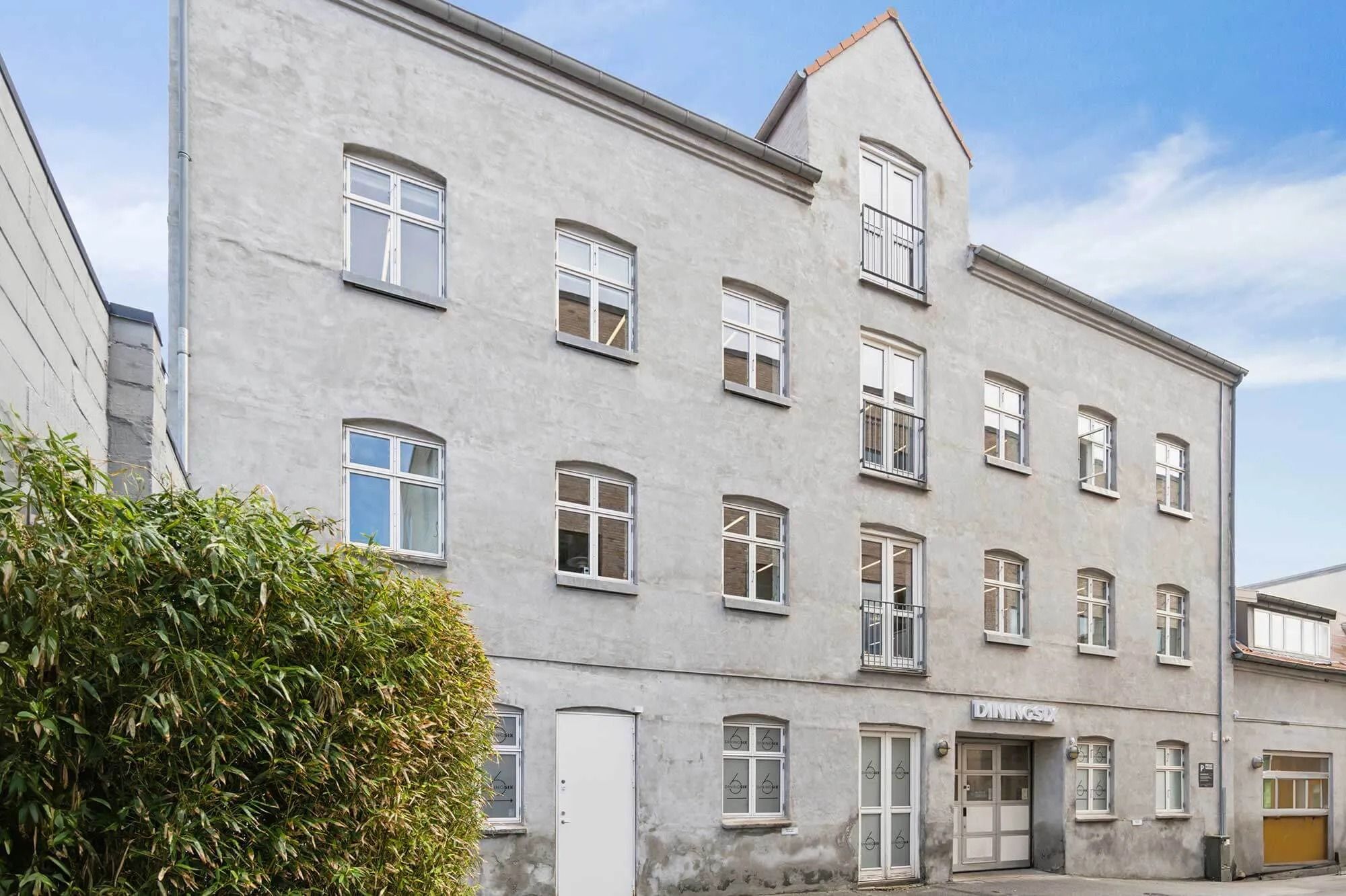 Moderne kontorbygning med lyse vinduer, hvide døre og store planter til siden