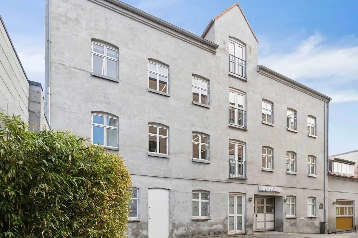 Moderne kontorbygning med lyse vinduer, hvide døre og store planter til siden