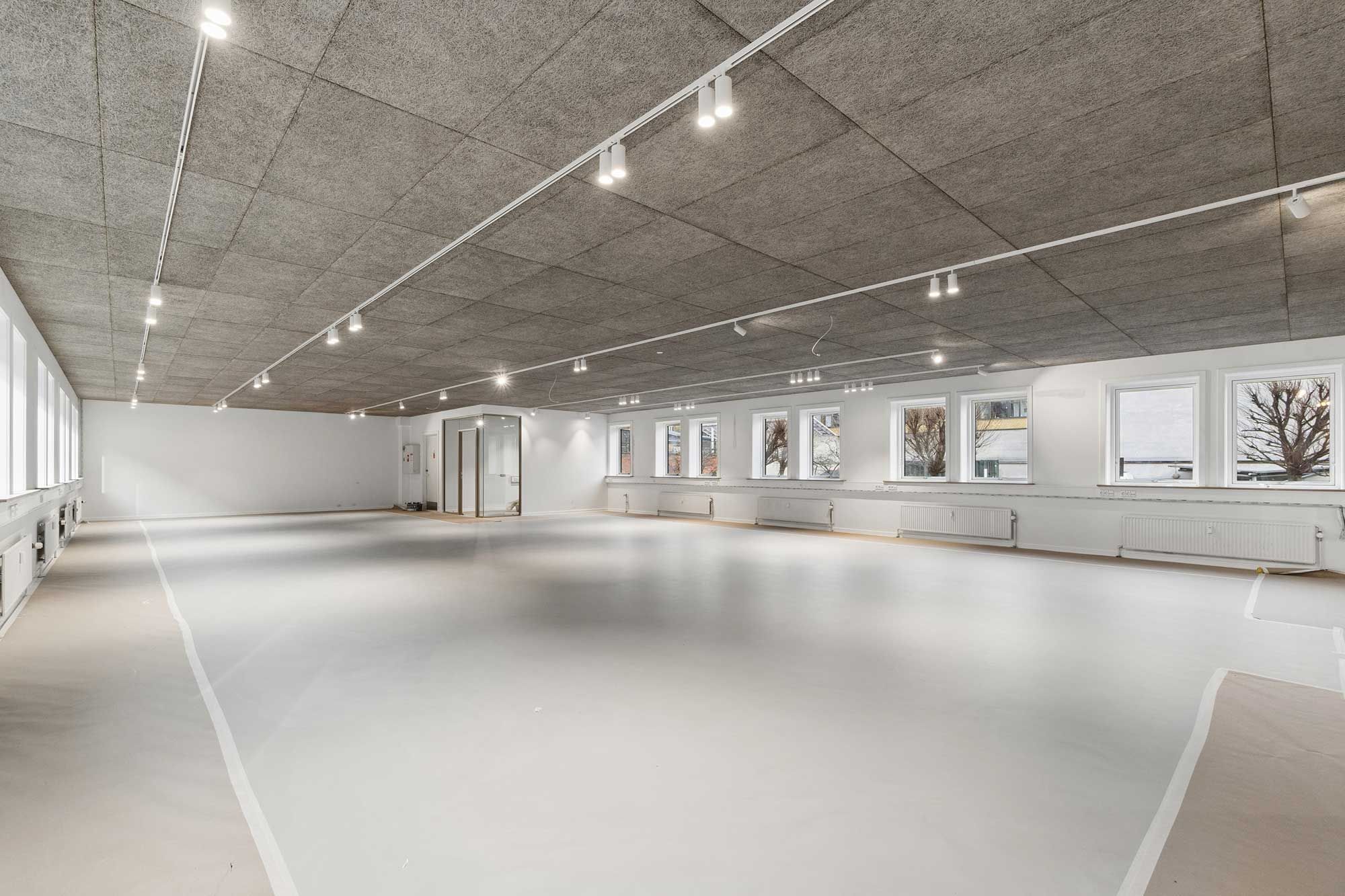 Store tomme rum med lyse loftslampe. Vinduer og hvide vægge. Trægulv og hvide linjer på gulvet.