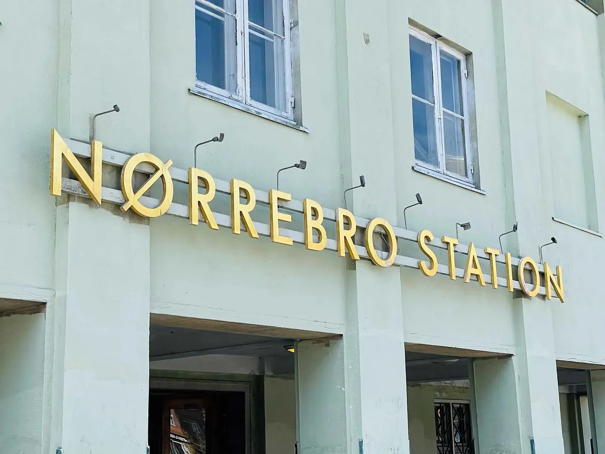 Lysgult skilt over indgangen til Nørrebro Station med lysekroner og vinduer i baggrunden