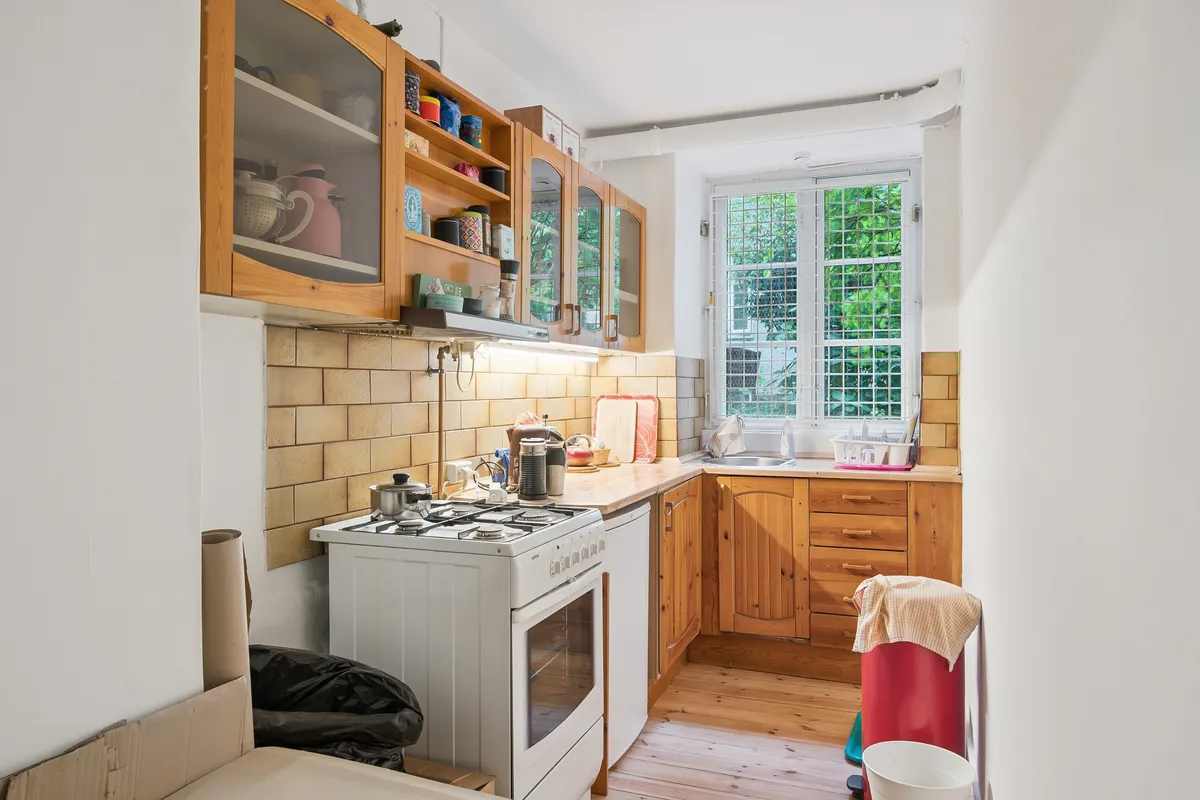 Lyst kælderlokale med lysegulle vægge, træskabe, hvid komfur, gaskomfur og vinduer ud mod grønne træer på den anden side af