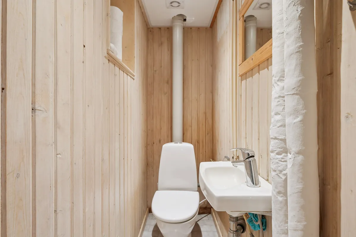 En lille toiletrum med hvide vægge og gulv samt et hvidt toilet og en hvid vaskehane med håndklæde.