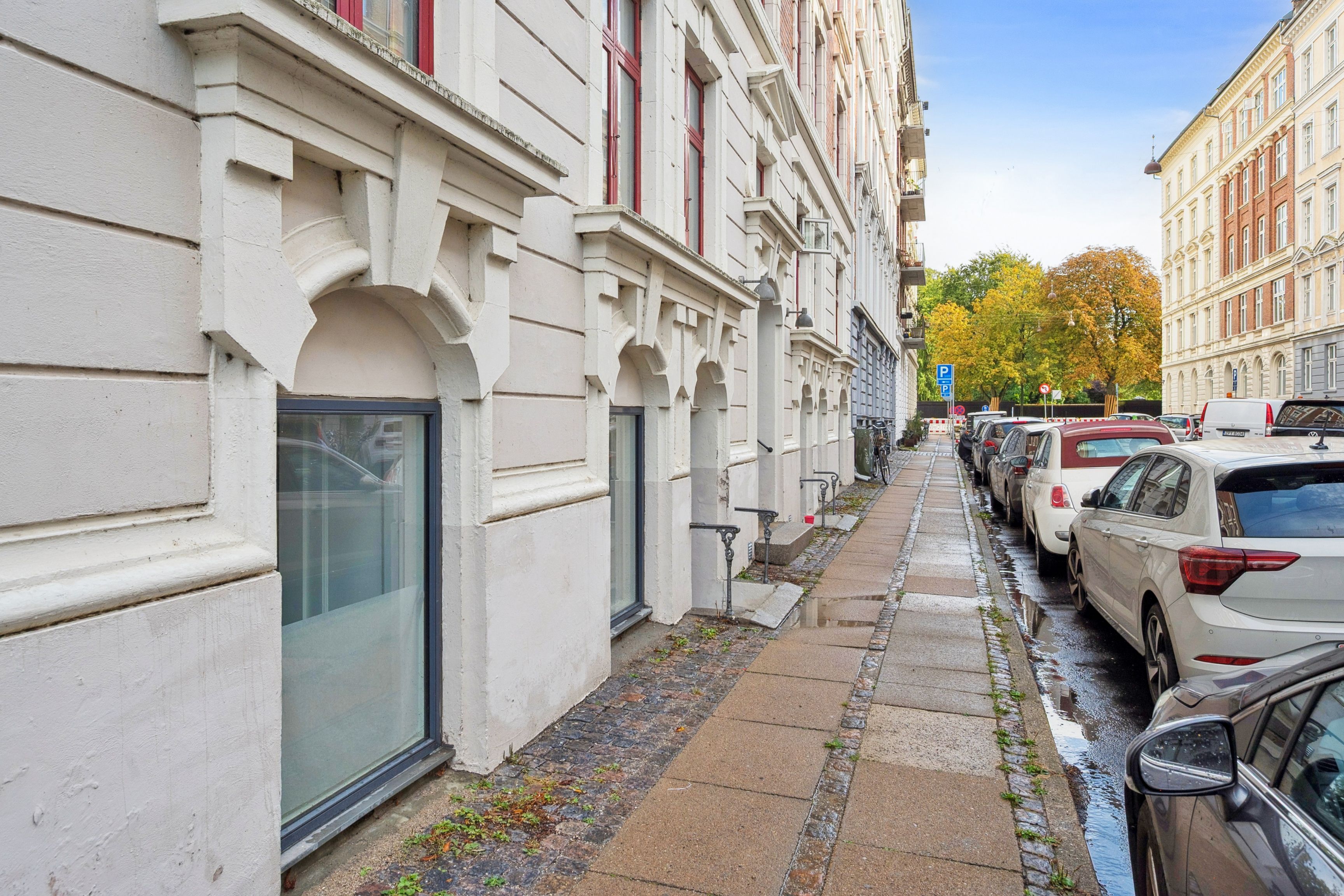 Lejemål med vinduer mod Collinsgade og parkerede biler langs gågaden, med et enkelt parkerede stel og en gult skilt