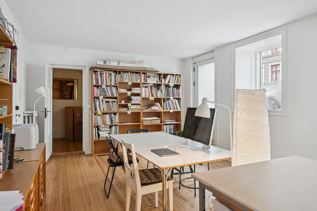 Moderne kontorlokale med højt kvalitetsmæssigt udstyr og møbler, herunder en stor bogreol, skrivebord og computere