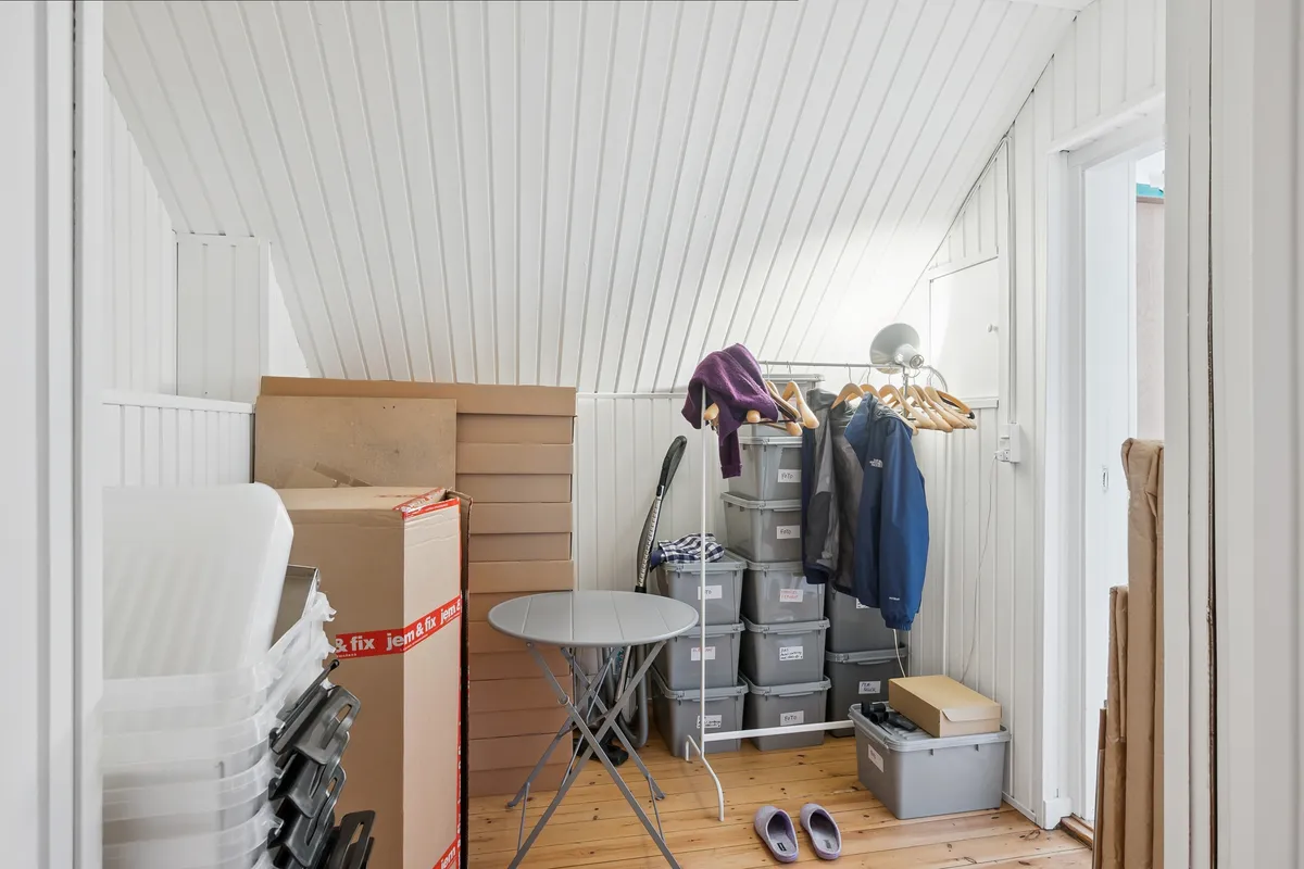 Et lille, lyst lager med flere kartoner og plastikkasser samt to par fodtøj og en lille rundt bord.