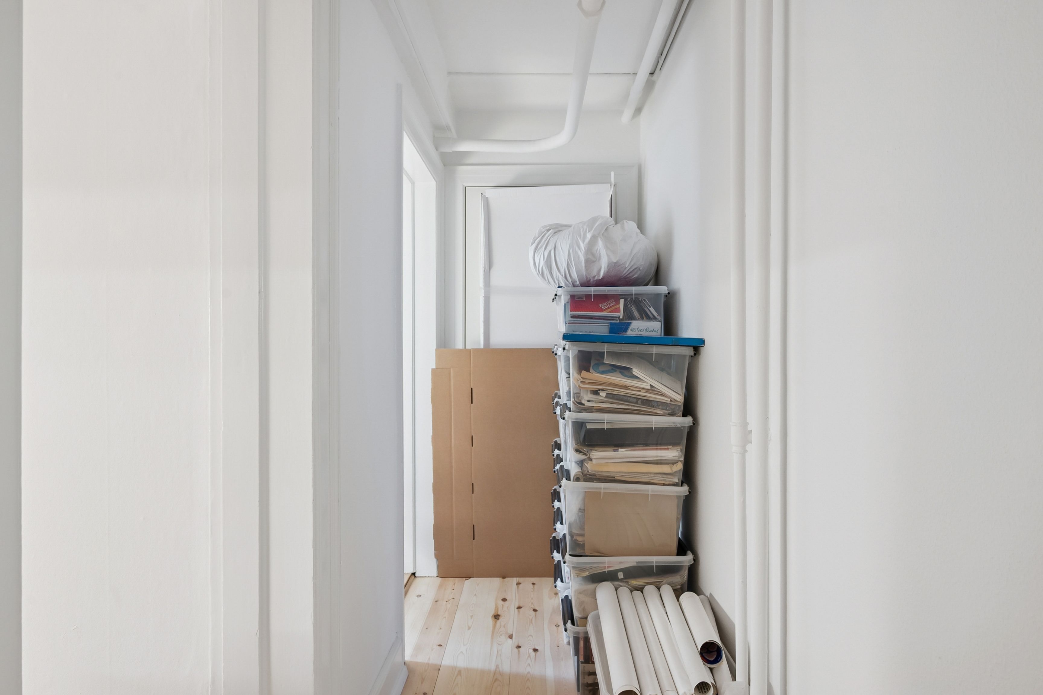 Ledig kælderlokale med flere lagerkasser, papkasser og plastposer. Kælderlokale har hvide vægge og trægulv