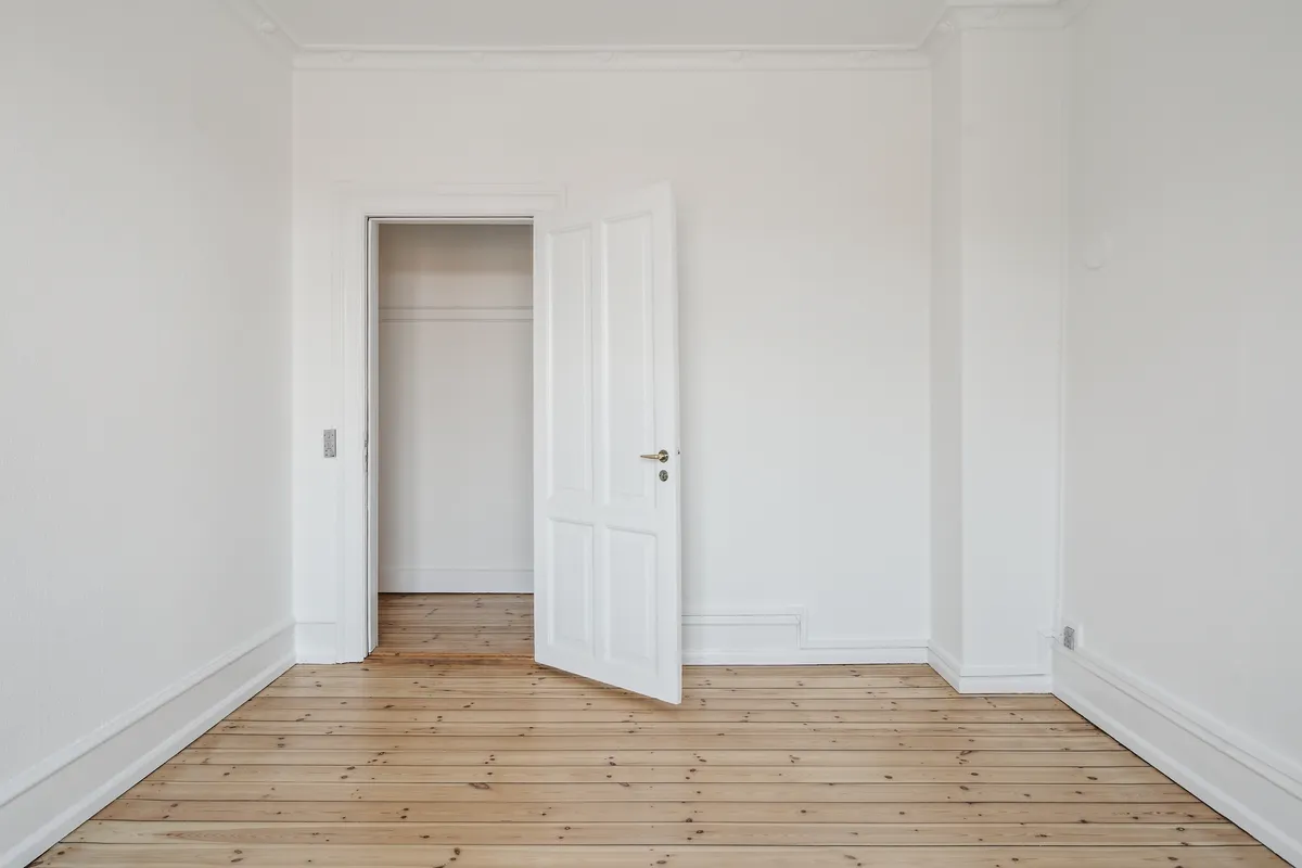 To hvide døre i hvidt rum med åbne døre og trægulv med lyse og mørke linjer