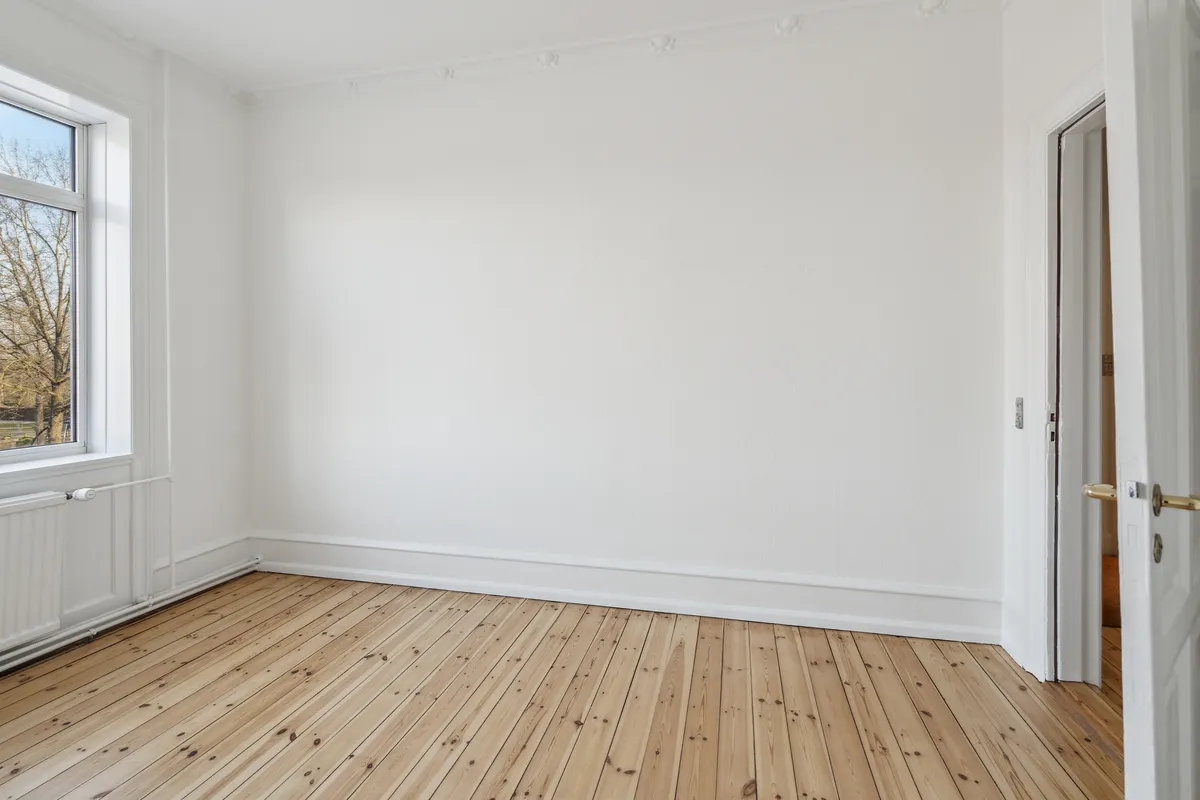 Et tomt og pænt kontorlokale med hvidt gulv og hvide vægge samt et glasvindue med udsigt til et træ udenfor