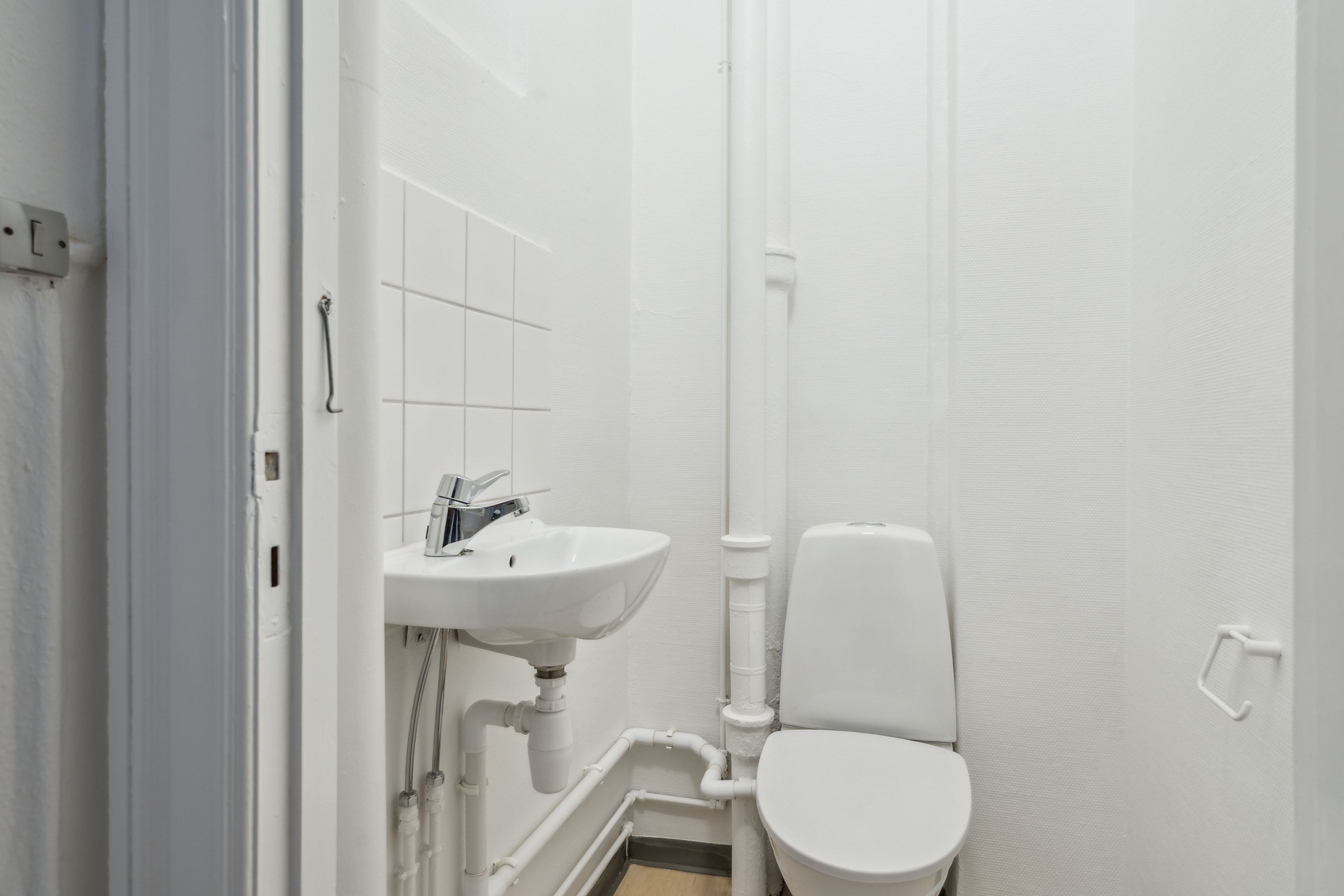 Et lille badeværelse med hvide vægge og et hvidt toilet med hvidt sæde og håndtag