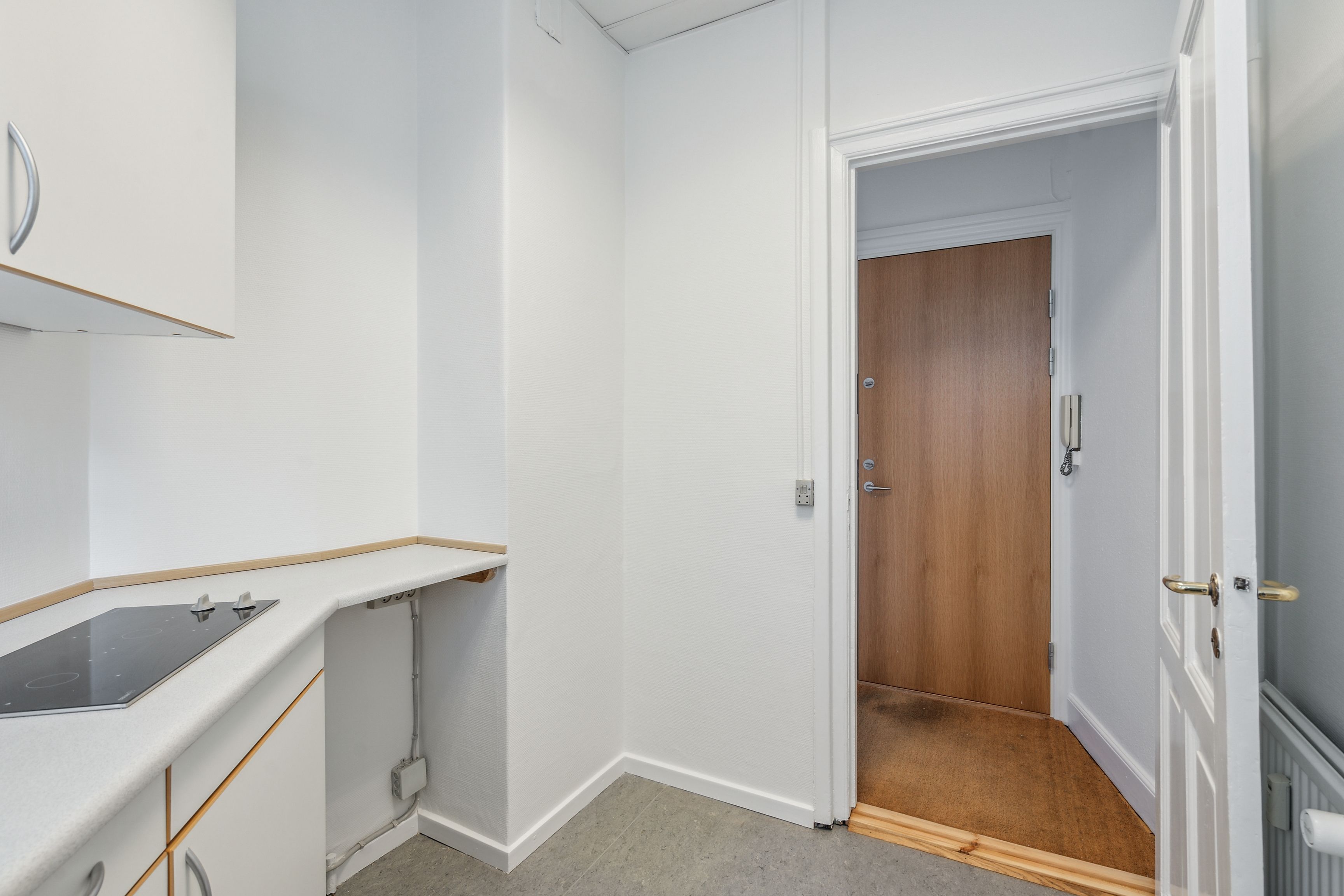 Minimalistisk køkken med induktionskomfur og hvide vægge, moderne og funktionel design med lyse hjørner og åbent træpanel på