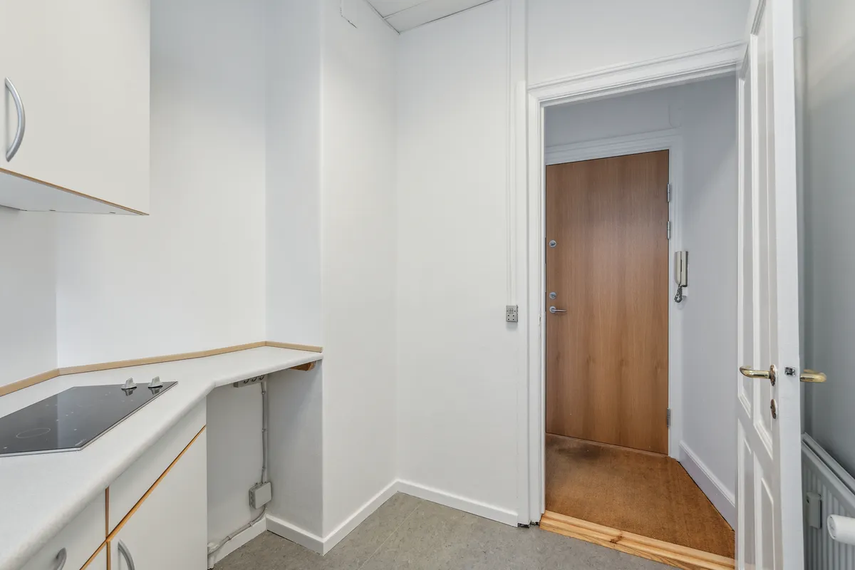 Minimalistisk køkken med induktionskomfur og hvide vægge, moderne og funktionel design med lyse hjørner og åbent træpanel på