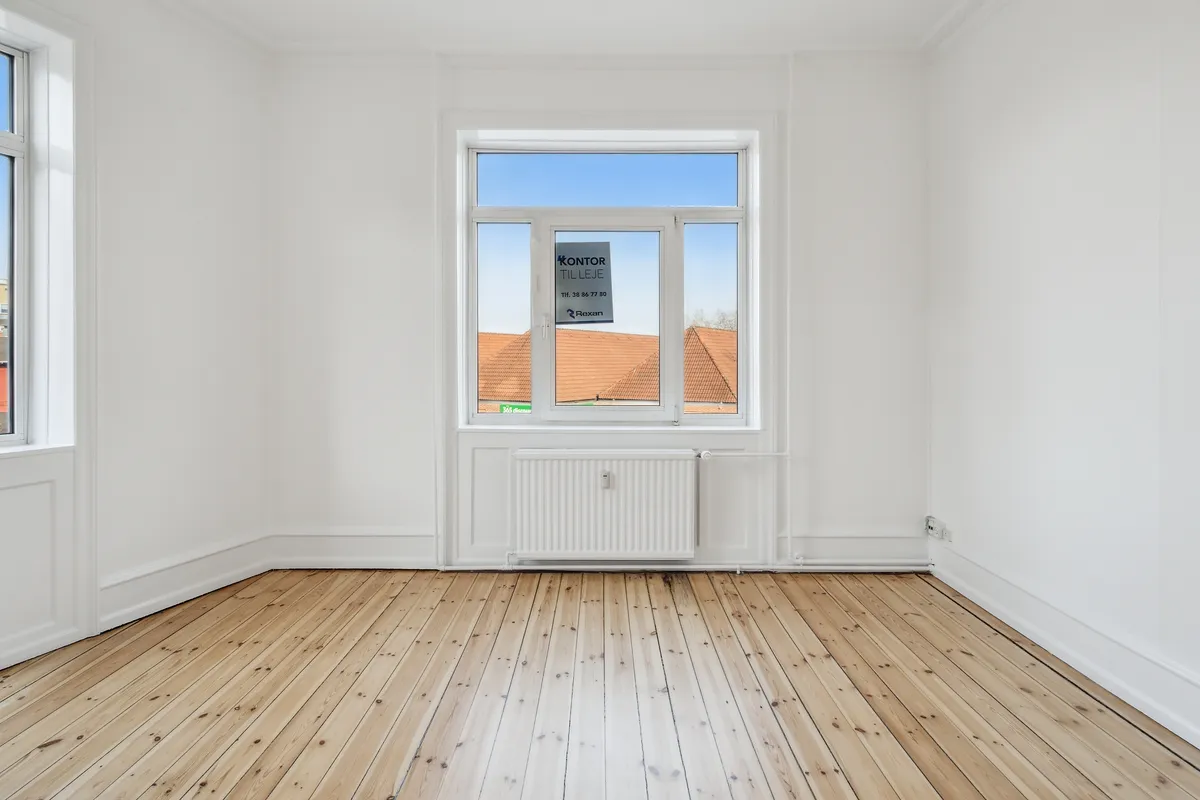 Lejlighed til leje i Taastrup med lyse gulve, hvide vægge og to store vinduer med slanke rammer og en åben udsigt til en