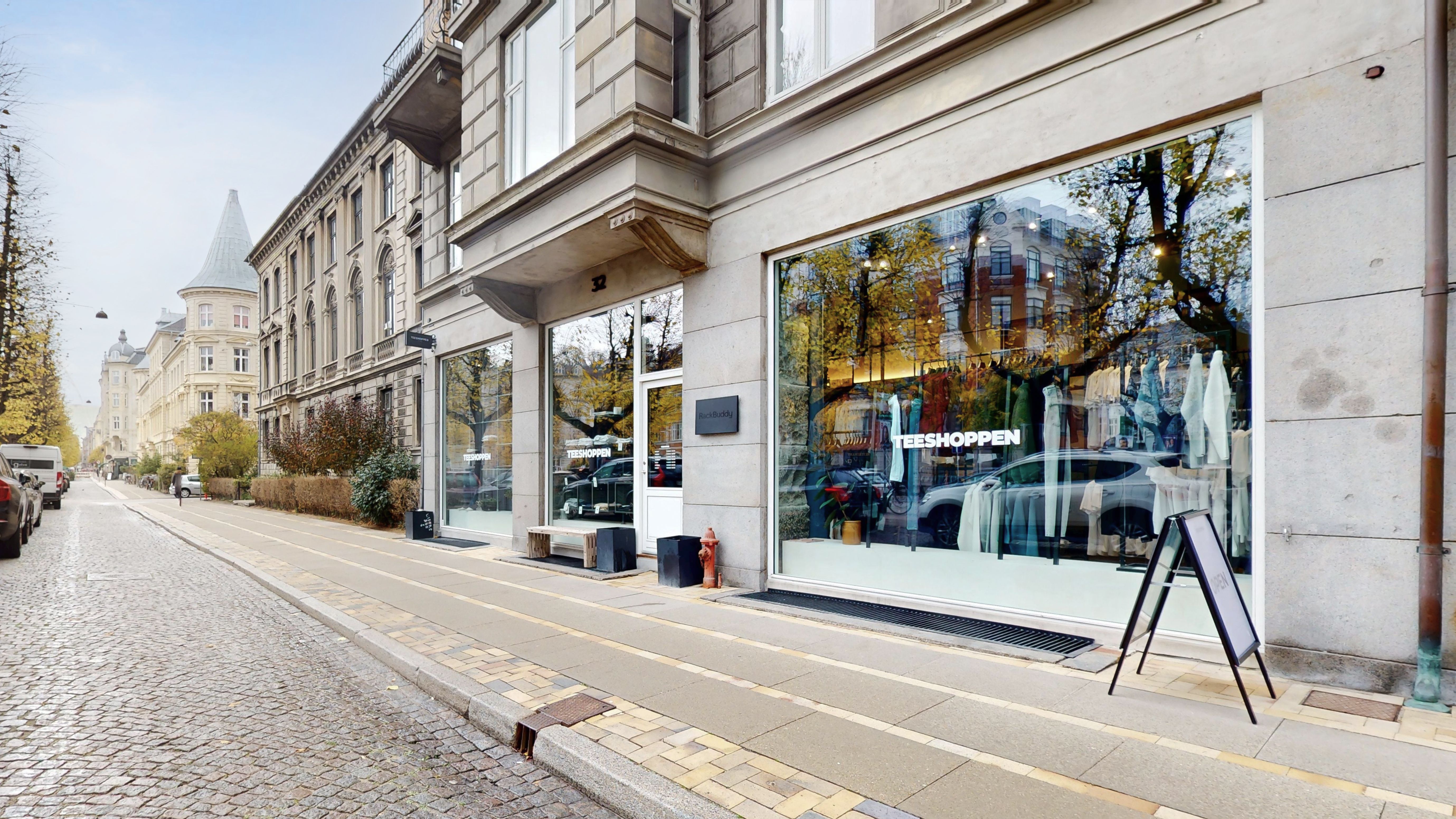 Tøjbutik med store ruder, hvor tøjet er udsat og en skrift på facaden læser Teeshoppen