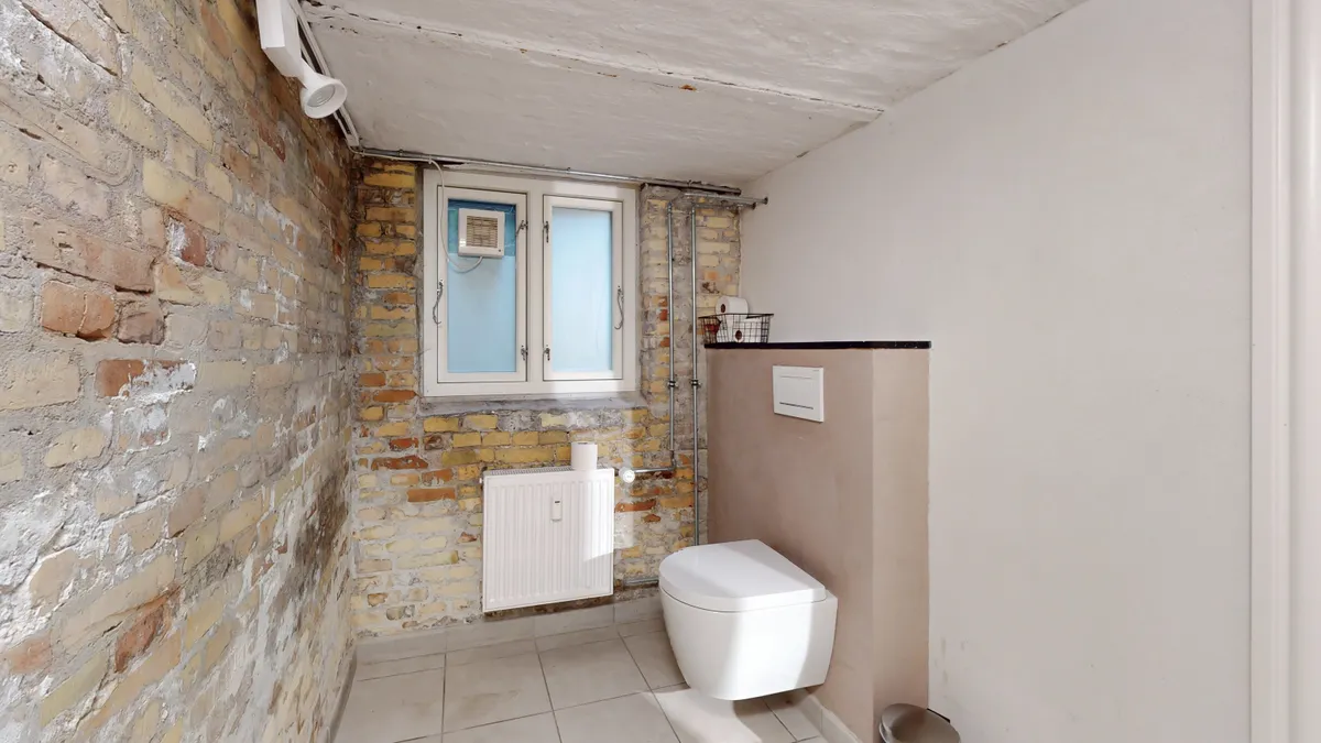 En toilet med lyse, moderne interiør, hvide keramiske toilet, og en lysegrå væg. En radiator er monteret på væggen, og der