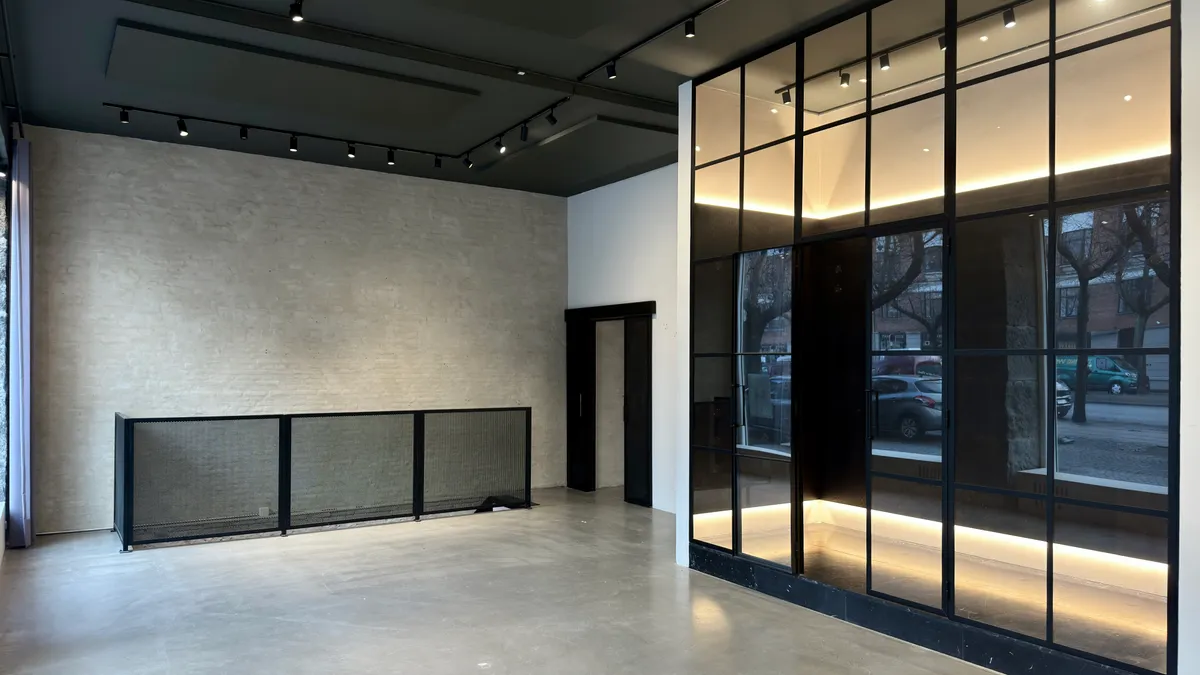 Store glasruder og mørke metalprofiler giver en moderne og elegant indgangszone til et kontorlokal med betongulv og lyse accenter på væggen