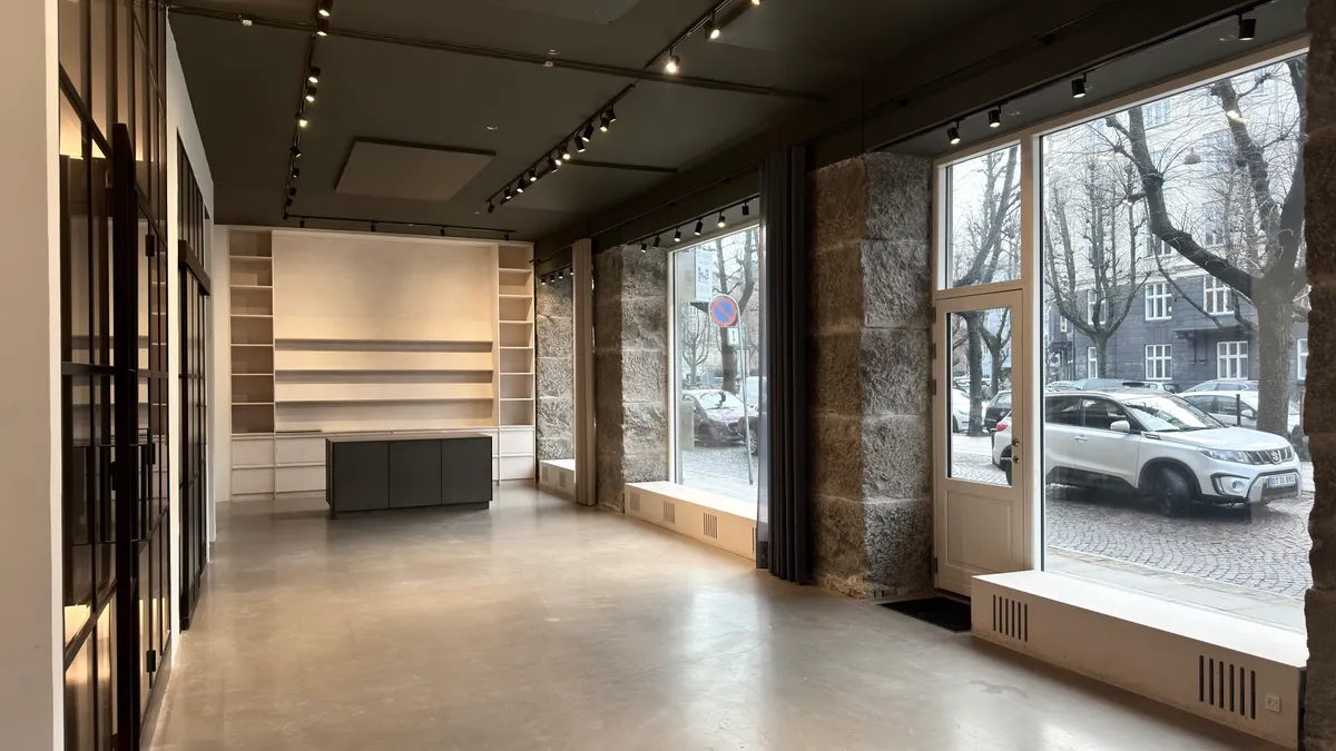 Indvendigt kontorlokaler med lyse gulve og højloftede rum. Væggene er udsmykket med store vinduer, som giver masser af naturlys. Der er en stor søjle og en lukket dør i baggrunden.