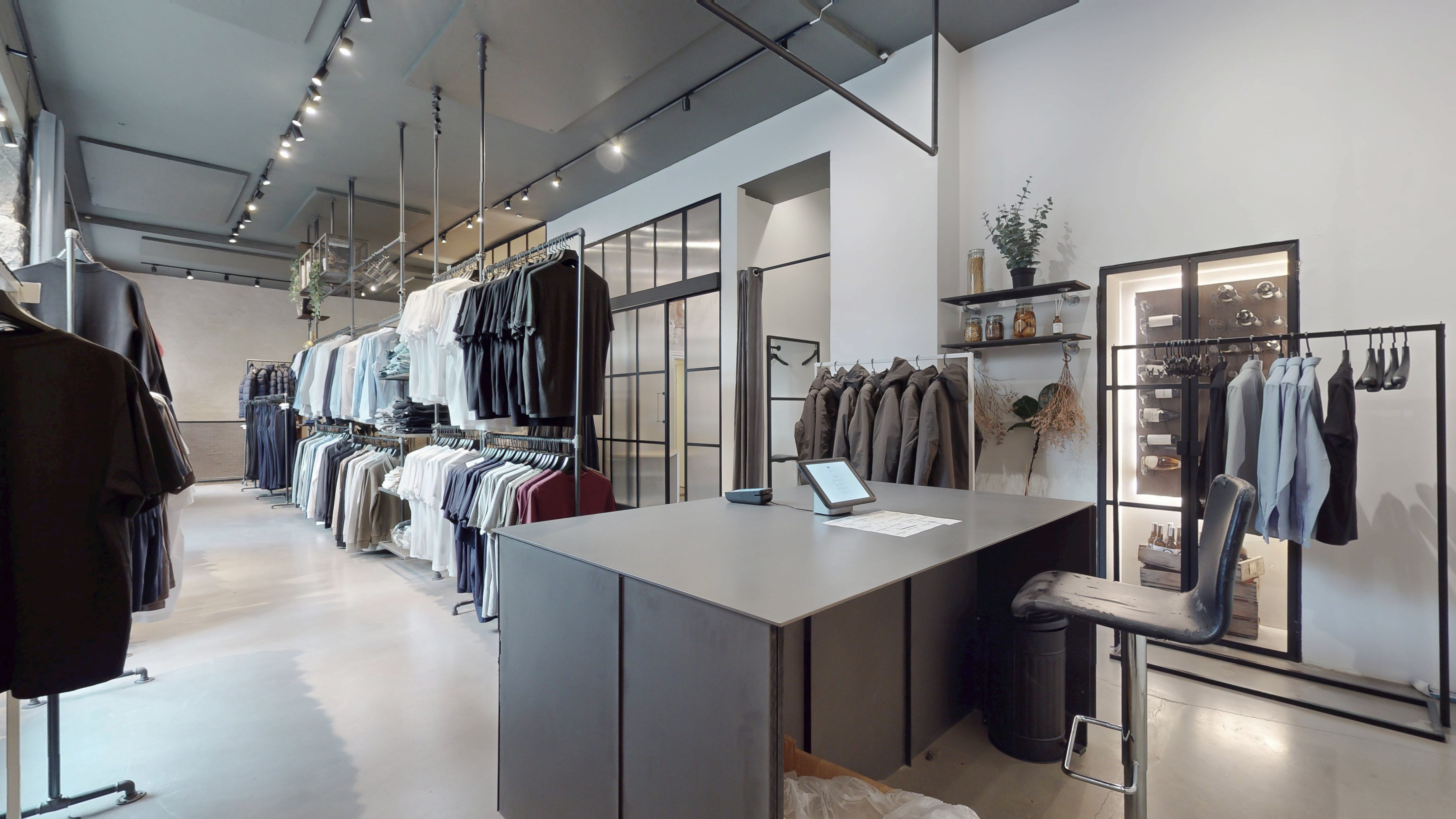 Modernt indrettet boutique med tøjskabe og hylder. Køkken med serveringsbord og træstol. Minimalistisk design med hvide