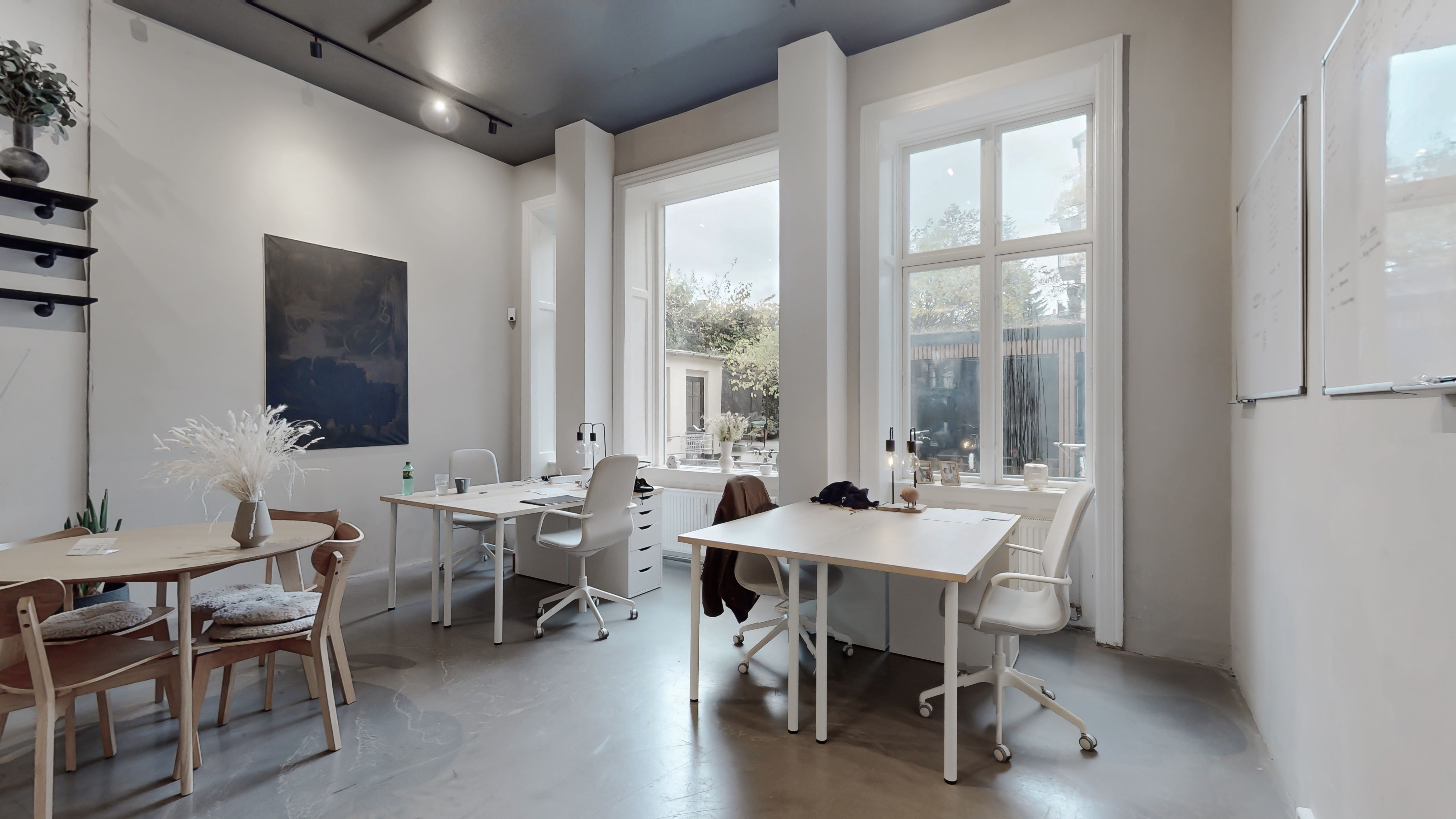 Hvidt og rent kontor med to skriveborde og stole samt et større skrivebord med to stole og plante på skrivebordet