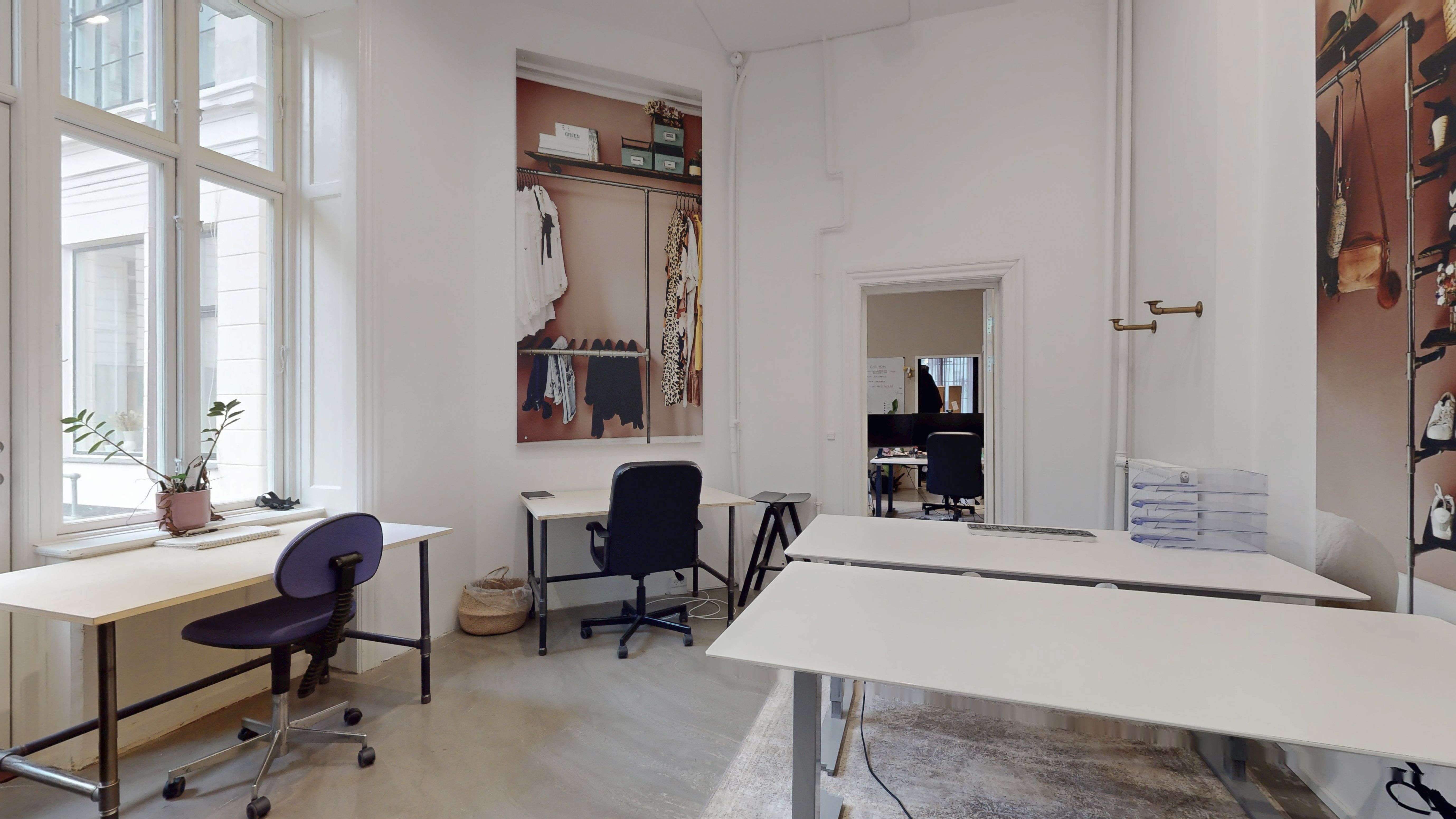 Kontorlokaler med lyse gulve og hvide vægge og skriveborde med stole og et plantepotte på vindueskærmen