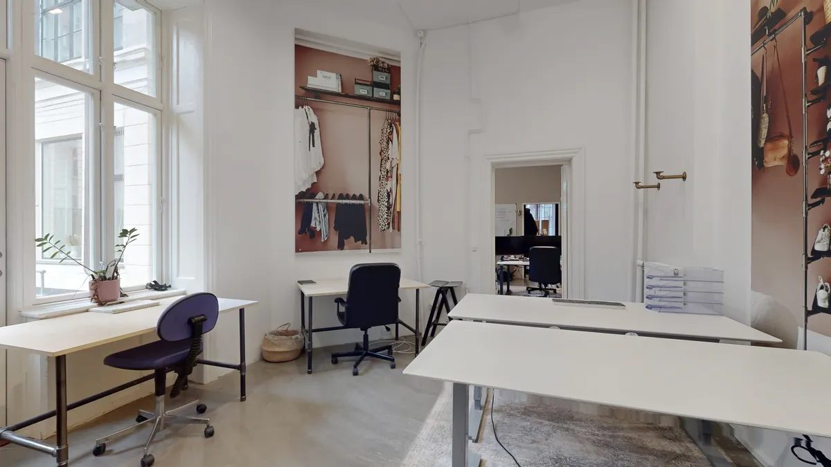 Kontorlokaler med lyse gulve og hvide vægge og skriveborde med stole og et plantepotte på vindueskærmen