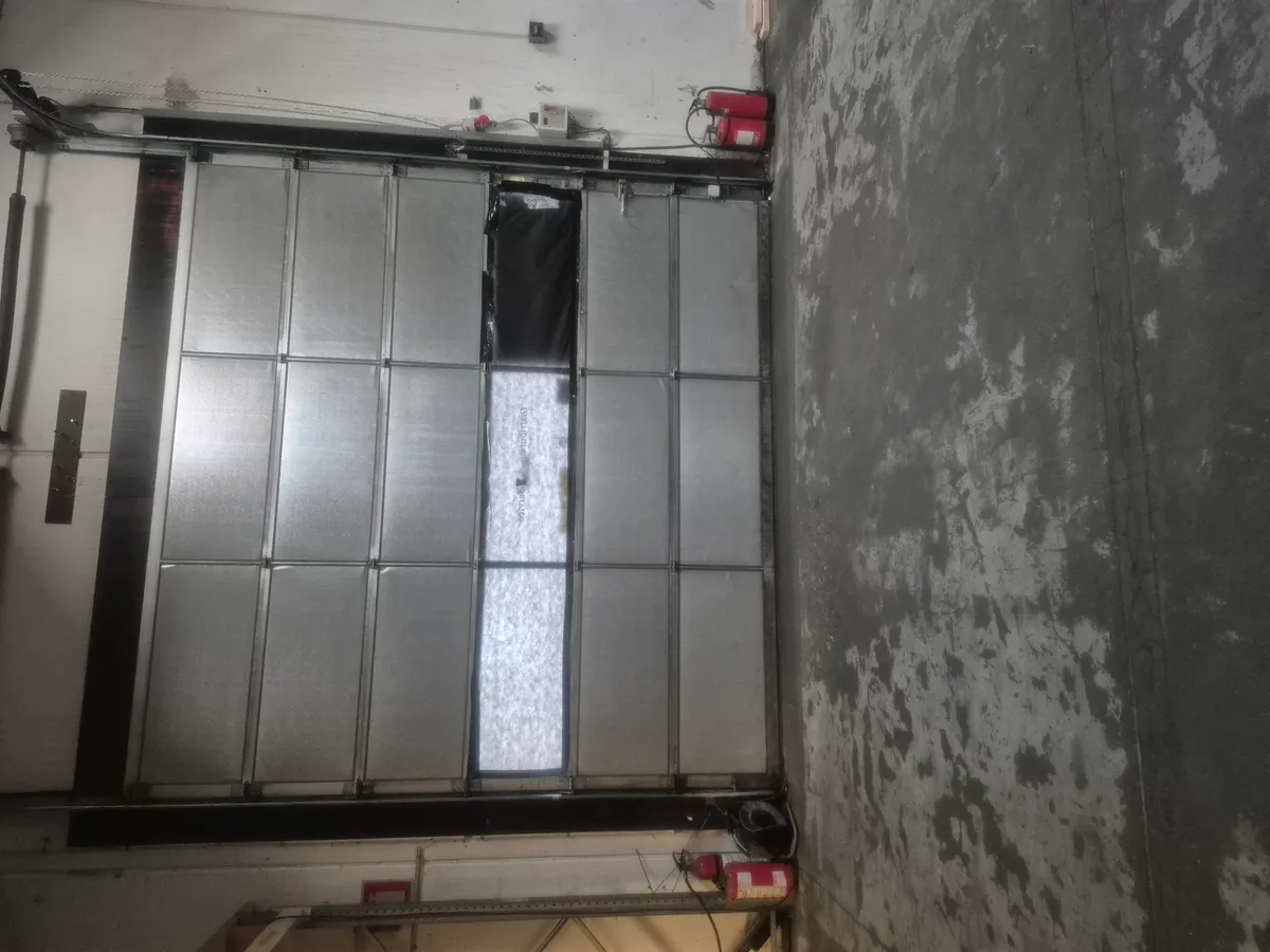 En stor metaldør med flere paneler og en lille åbning i midten og to brandustyr placeret på væggen