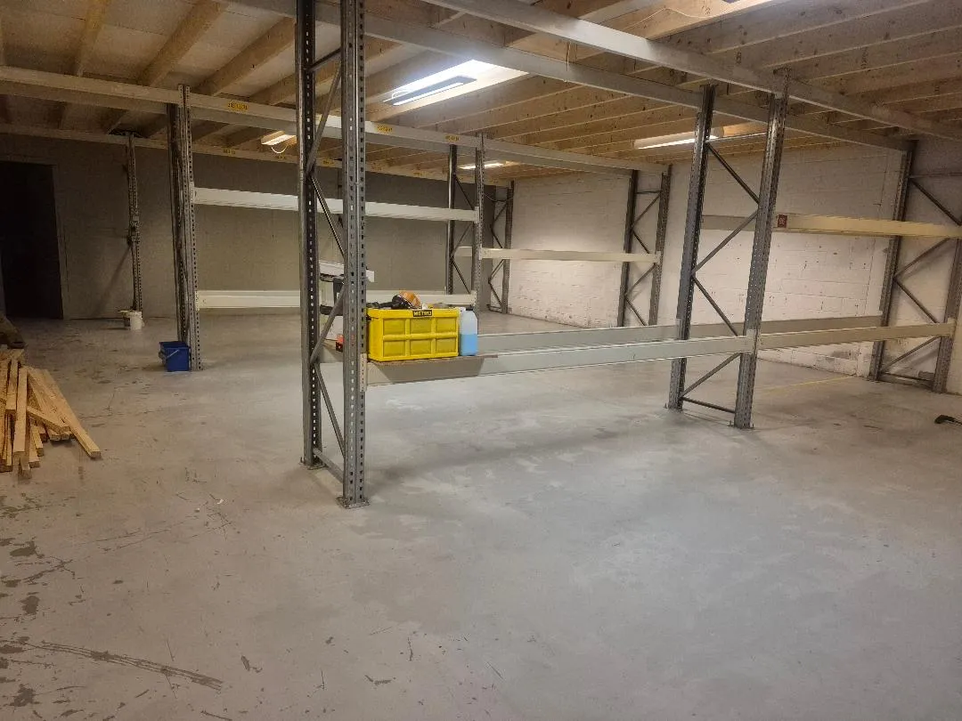 Et lager med store gulvlagerreoler og paller, samt brædder og en opladningsstation på gulvet.