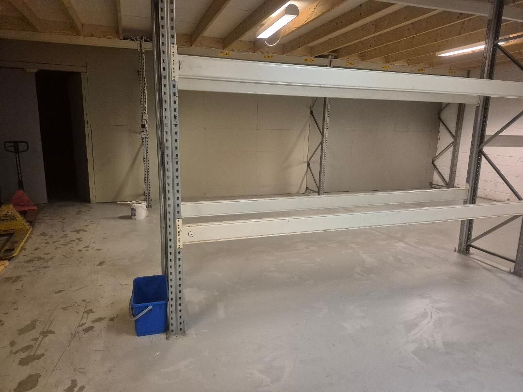 Lager med stålreoler og hvide loftsbjælker og gulve. Mærkbart ny og rent lager med højtloft og lys.