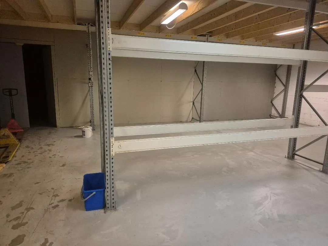 Lager med stålreoler og hvide loftsbjælker og gulve. Mærkbart ny og rent lager med højtloft og lys.