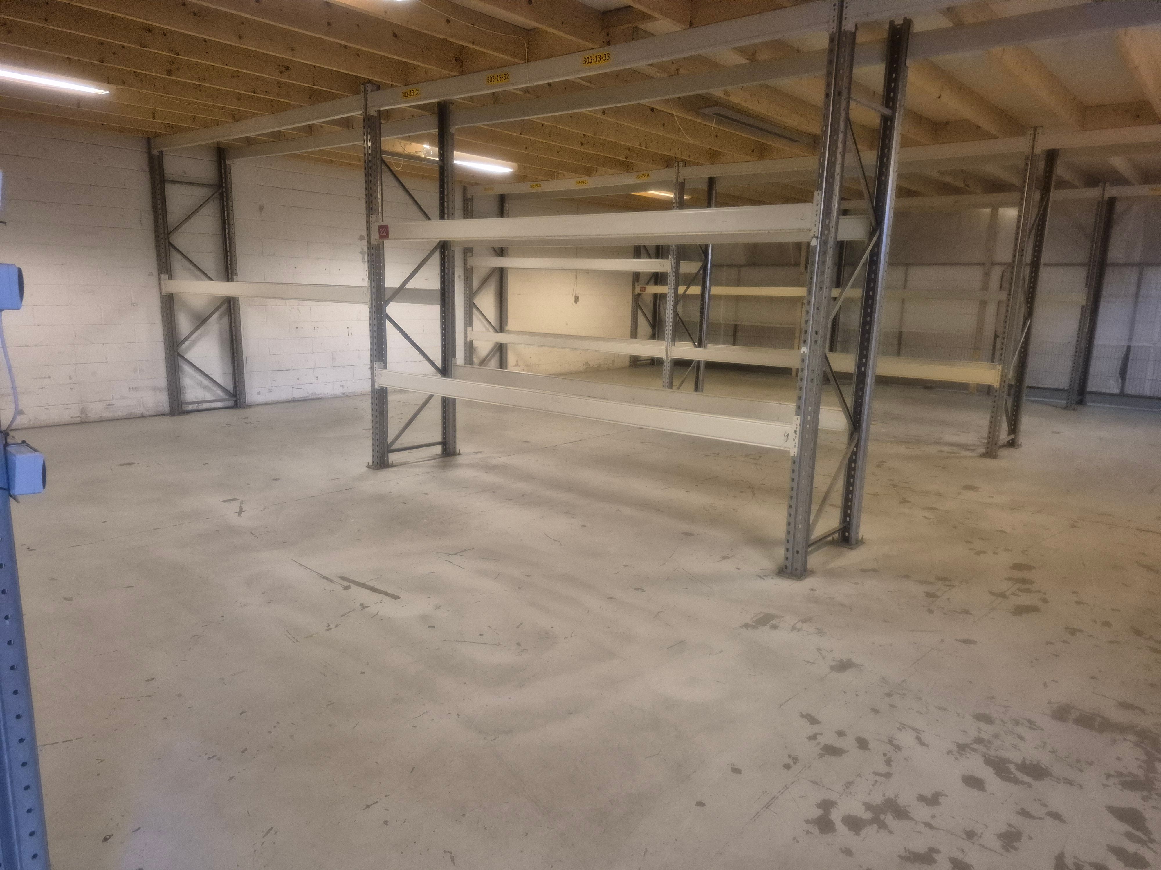 Lager med store metalhylder og gulv til lagerformål samt lys på loftet og en hvid mur