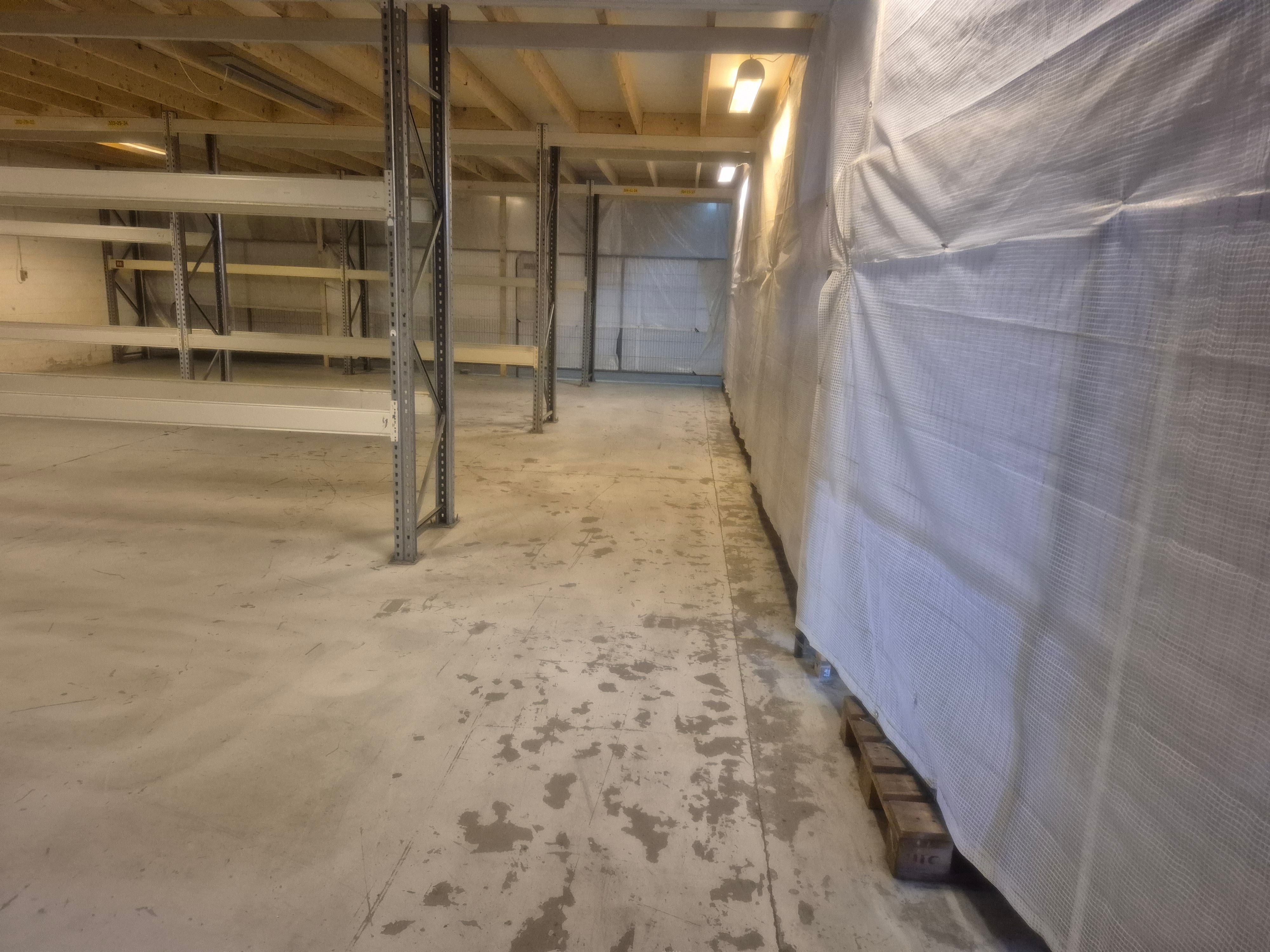 Lager med metalliske stativer og højloft, forseglet med hvide plastposer og lys på loftet, gulvet med spredte pletter