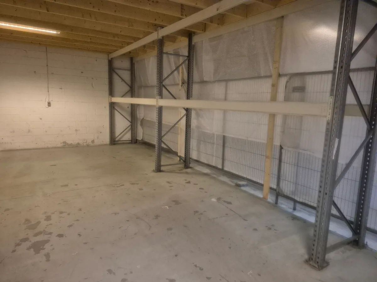 Lager med metalliske reoler og indvendigt parkeringsområde til vogn og lastbil, gulv og vægge i lysgrå maling