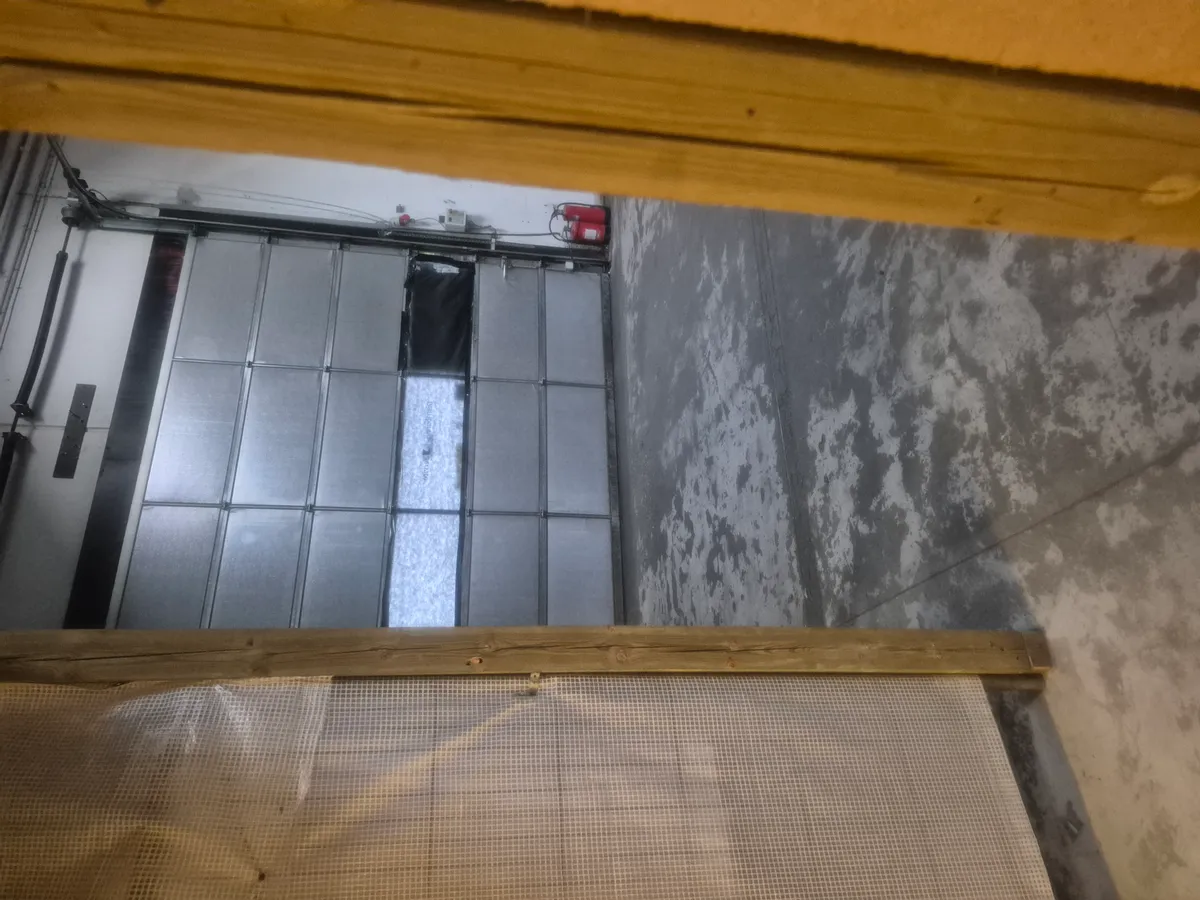 Glasdør i garage med rødt brandslukker og skraldkasse samt et stykke netværk uden for døren