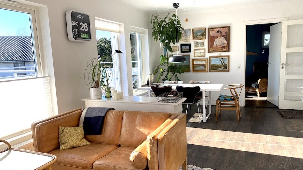 Et moderne interiør med en hvid sofa, lysegule pude og brune læderbeklædninger, møbler og en digital ur med dato.