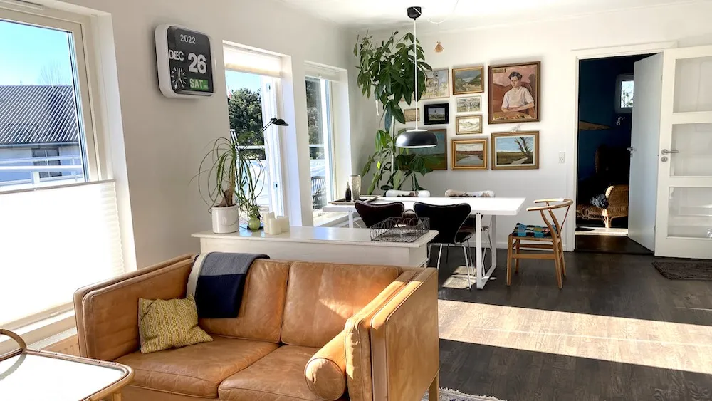 Et moderne interiør med en hvid sofa, lysegule pude og brune læderbeklædninger, møbler og en digital ur med dato.