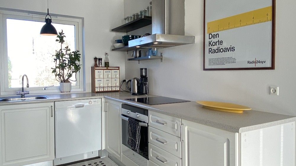 Rent, moderne køkken med hvide skabe og grå arbejdsbord. Der er et gult fade på arbejdsbordet og en kedel og en kaffemaskine