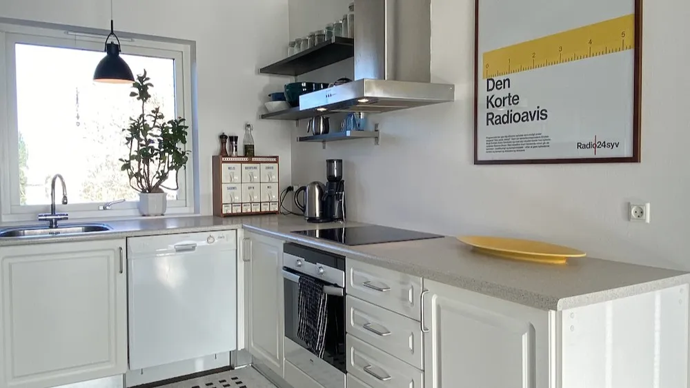 Rent, moderne køkken med hvide skabe og grå arbejdsbord. Der er et gult fade på arbejdsbordet og en kedel og en kaffemaskine