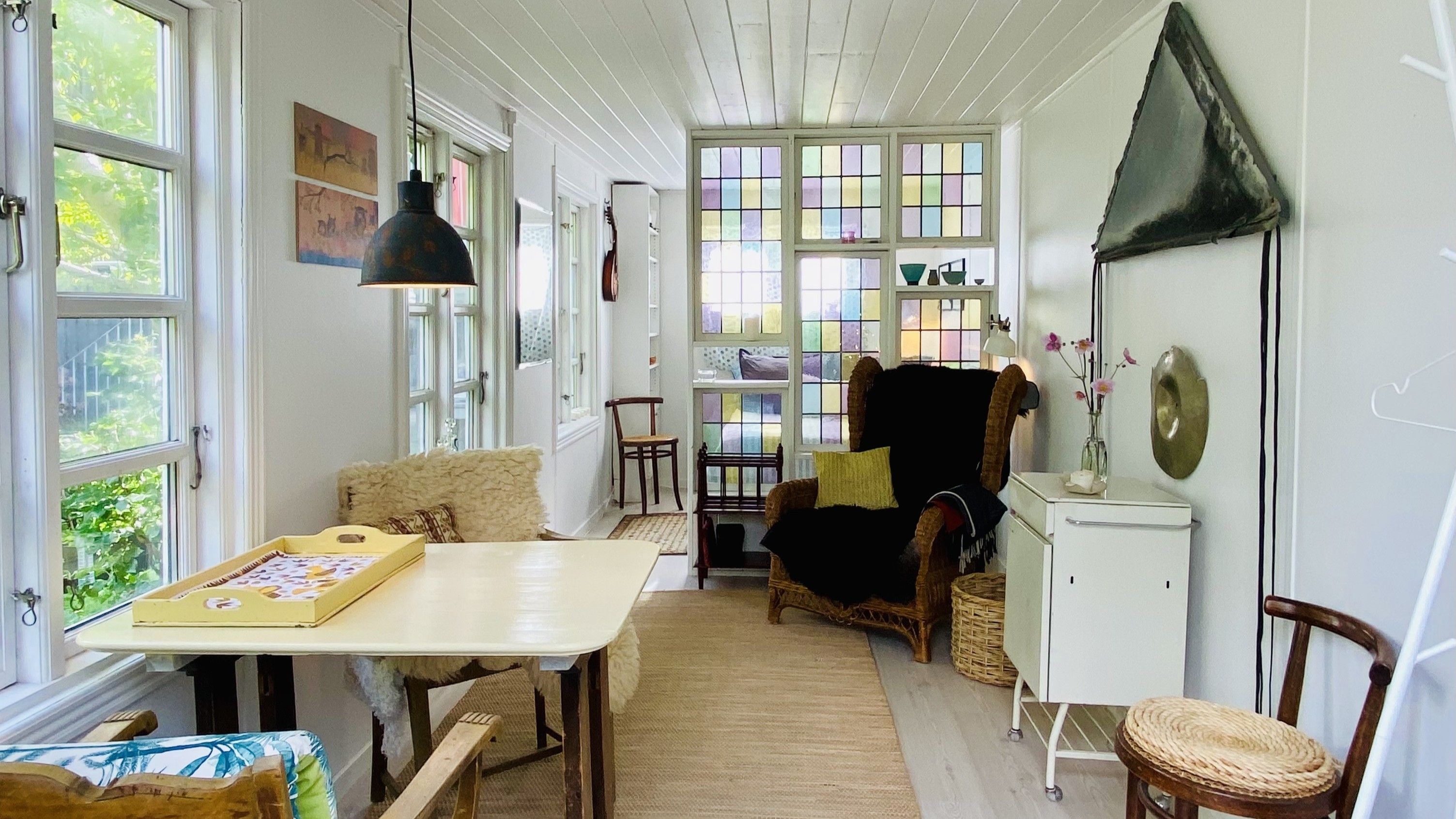 Inde i en lejlighed med lyse gulvvægge og hvide vægge. Et træbord med et træfad med en plade og et køkken. Et soveværelse