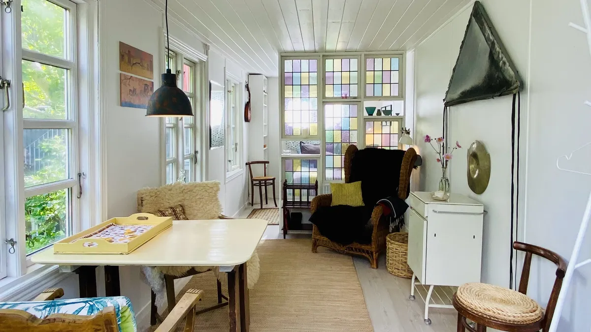 Inde i en lejlighed med lyse gulvvægge og hvide vægge. Et træbord med et træfad med en plade og et køkken. Et soveværelse