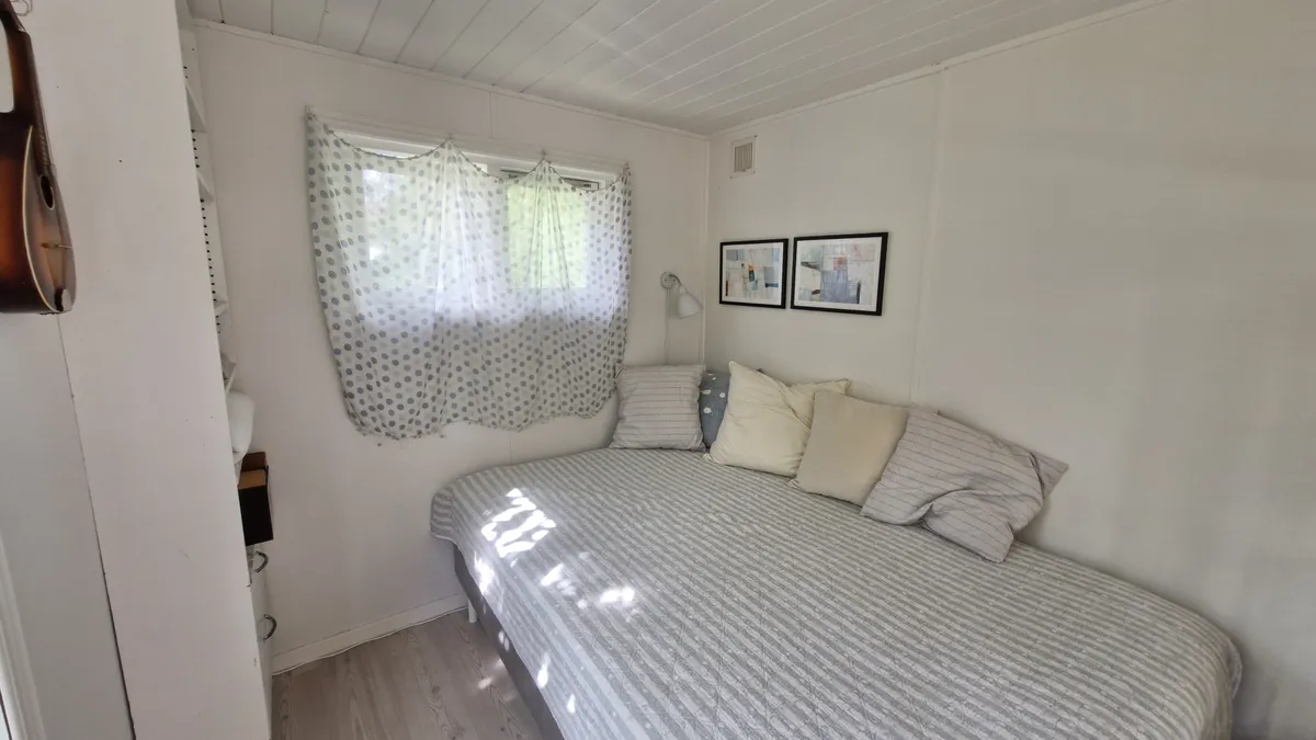 Et soveværelse med en seng og puderne, to malerier og et vinduesgardin med lyst gennem det.